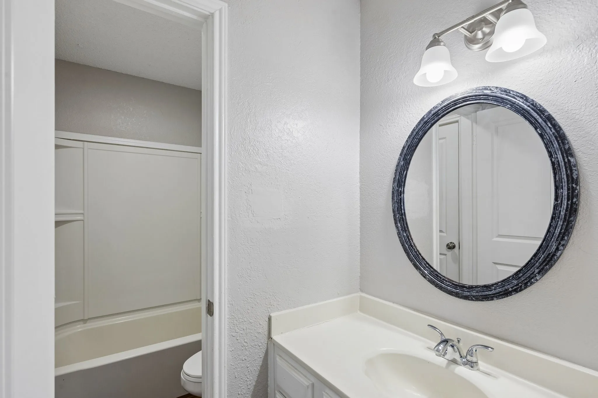 Bathroom vanity with a white countertop and oval undermount sink, complemented by a round mirror with a textured frame