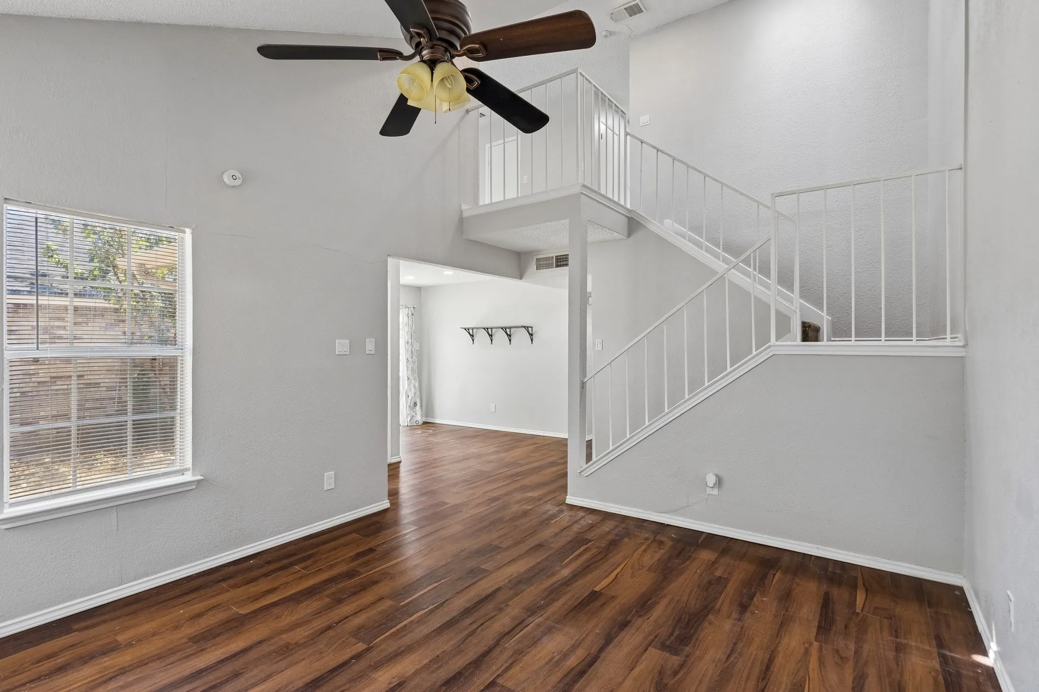 Vaulted ceiling with a ceiling fan, wood-finish flooring, and white railing staircase