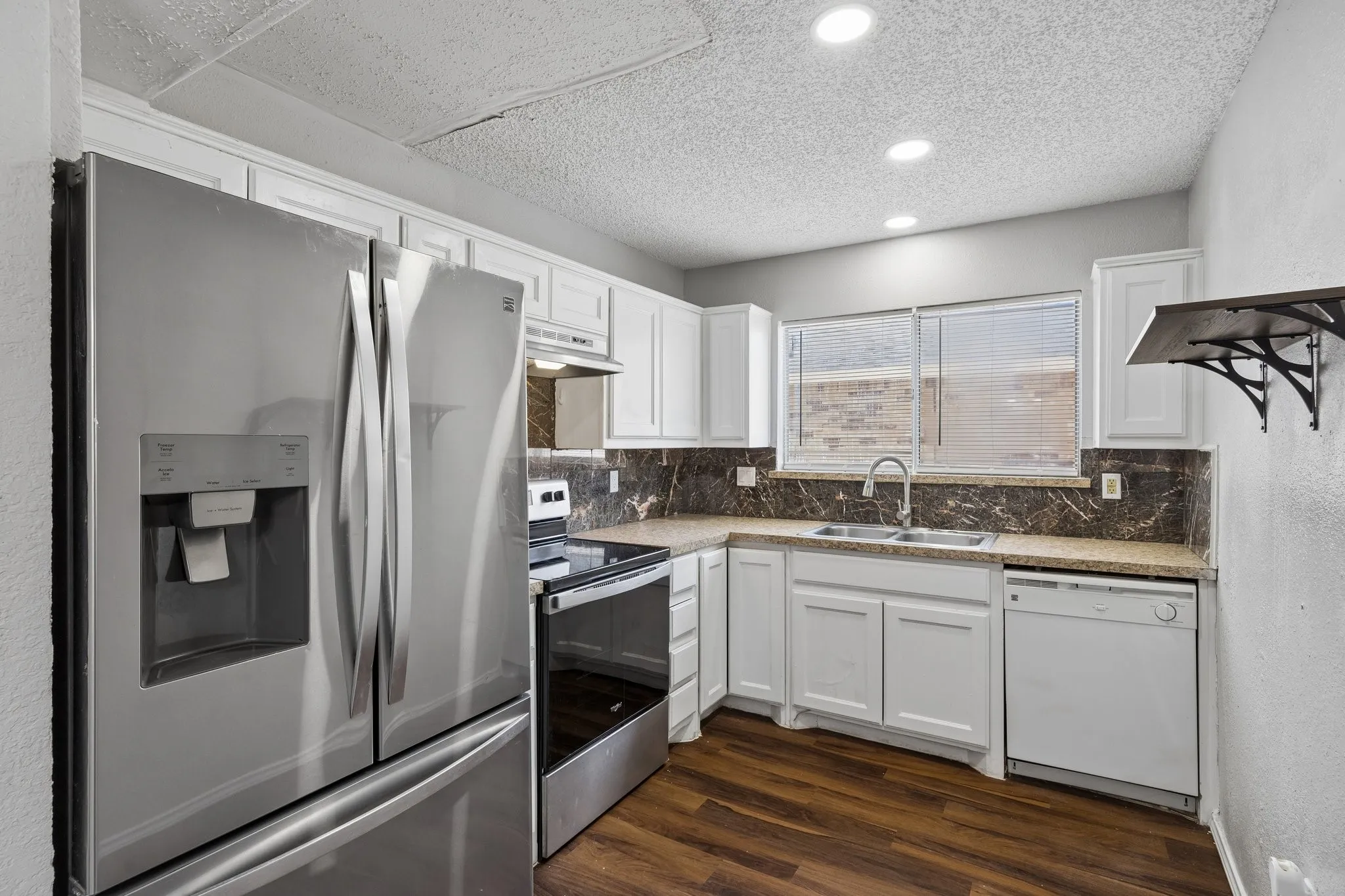 White shaker-style cabinetry, stainless steel French door refrigerator, built-in dishwasher, wood-finish flooring, recessed lighting