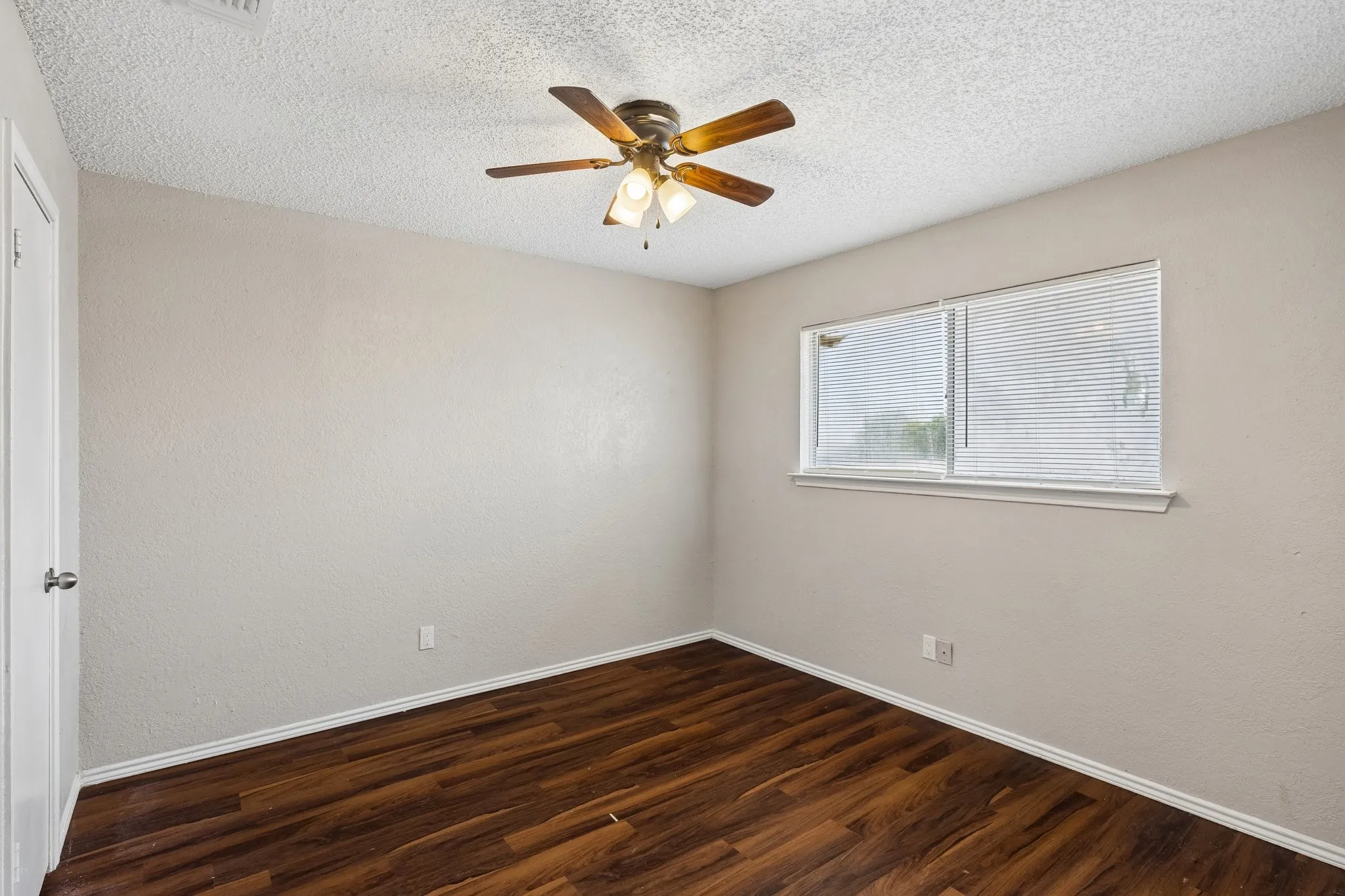 Bright corner bedroom with rich wood-finish flooring, ceiling fan with integrated lighting, and dual windows providing natural light