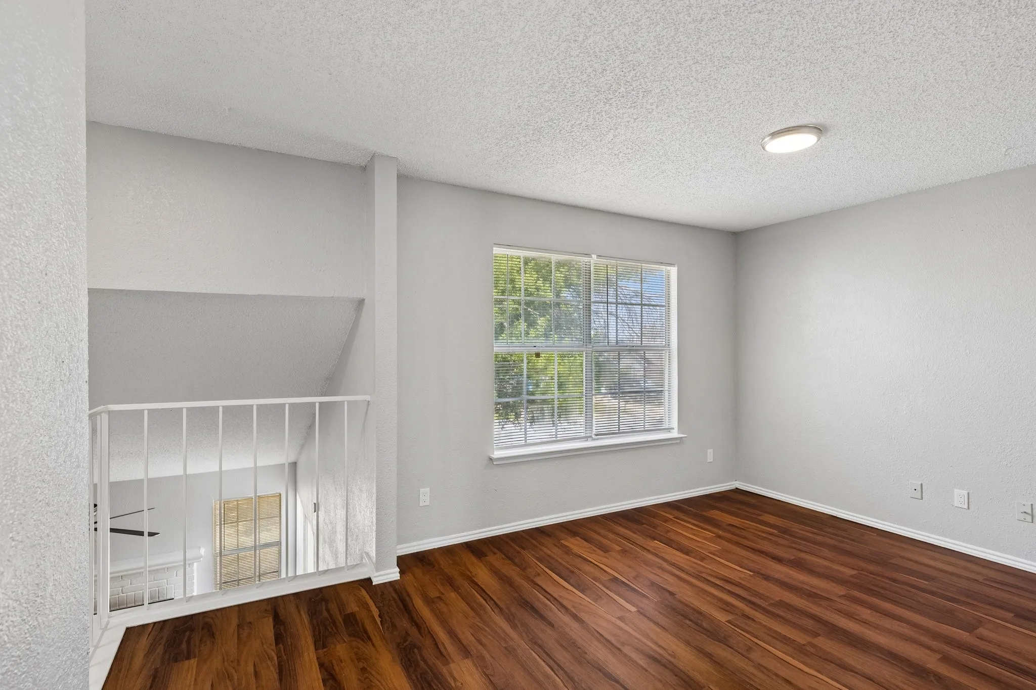 Wood-finish flooring, white wall railing, window with exterior landscape, flush-mount ceiling light, and light gray wall finish