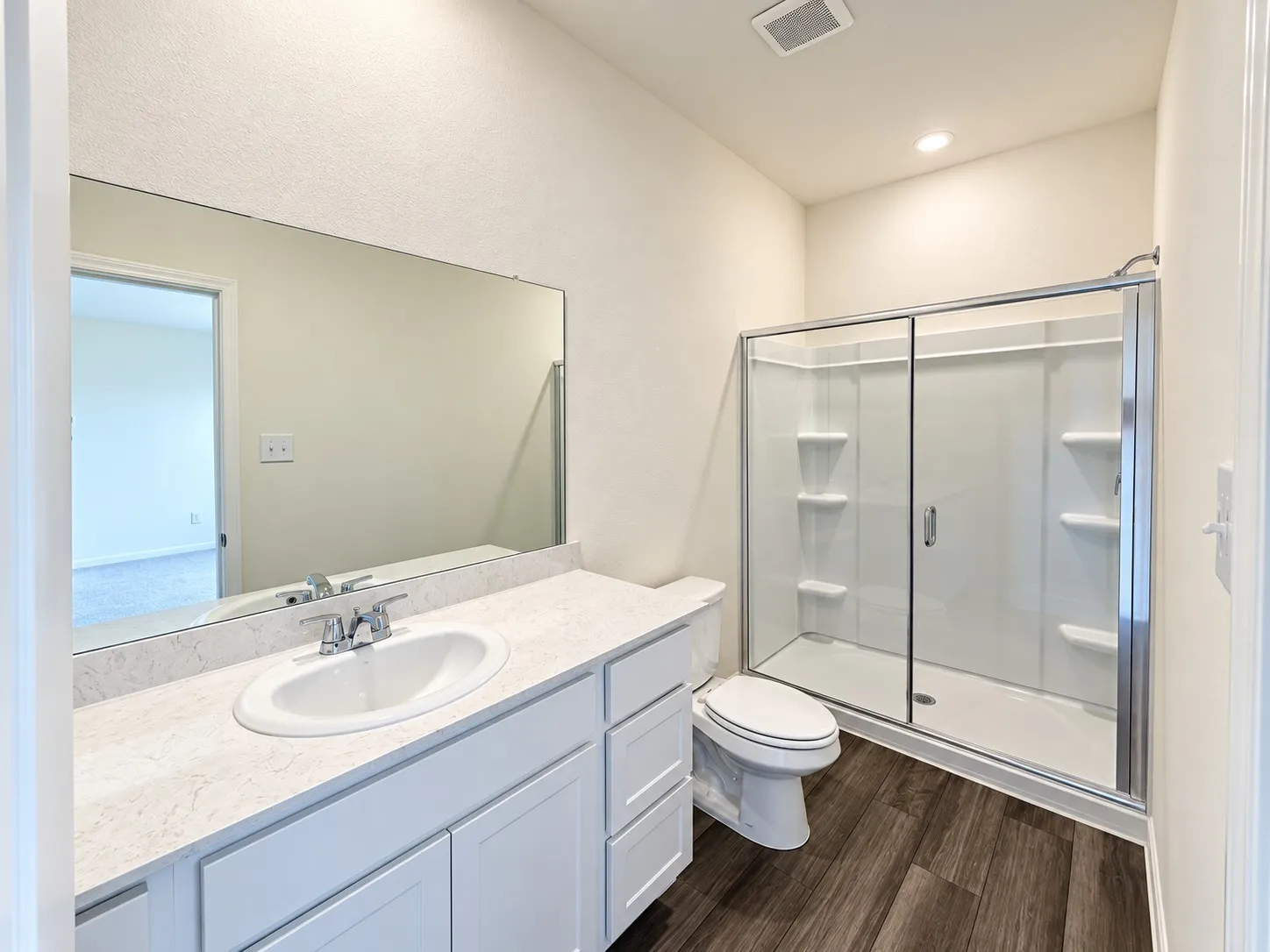 Bathroom featuring a white vanity with an undermount sink, a light-toned countertop, a frameless mirror, wood-finish flooring, and a glass-enclosed shower with white shelving