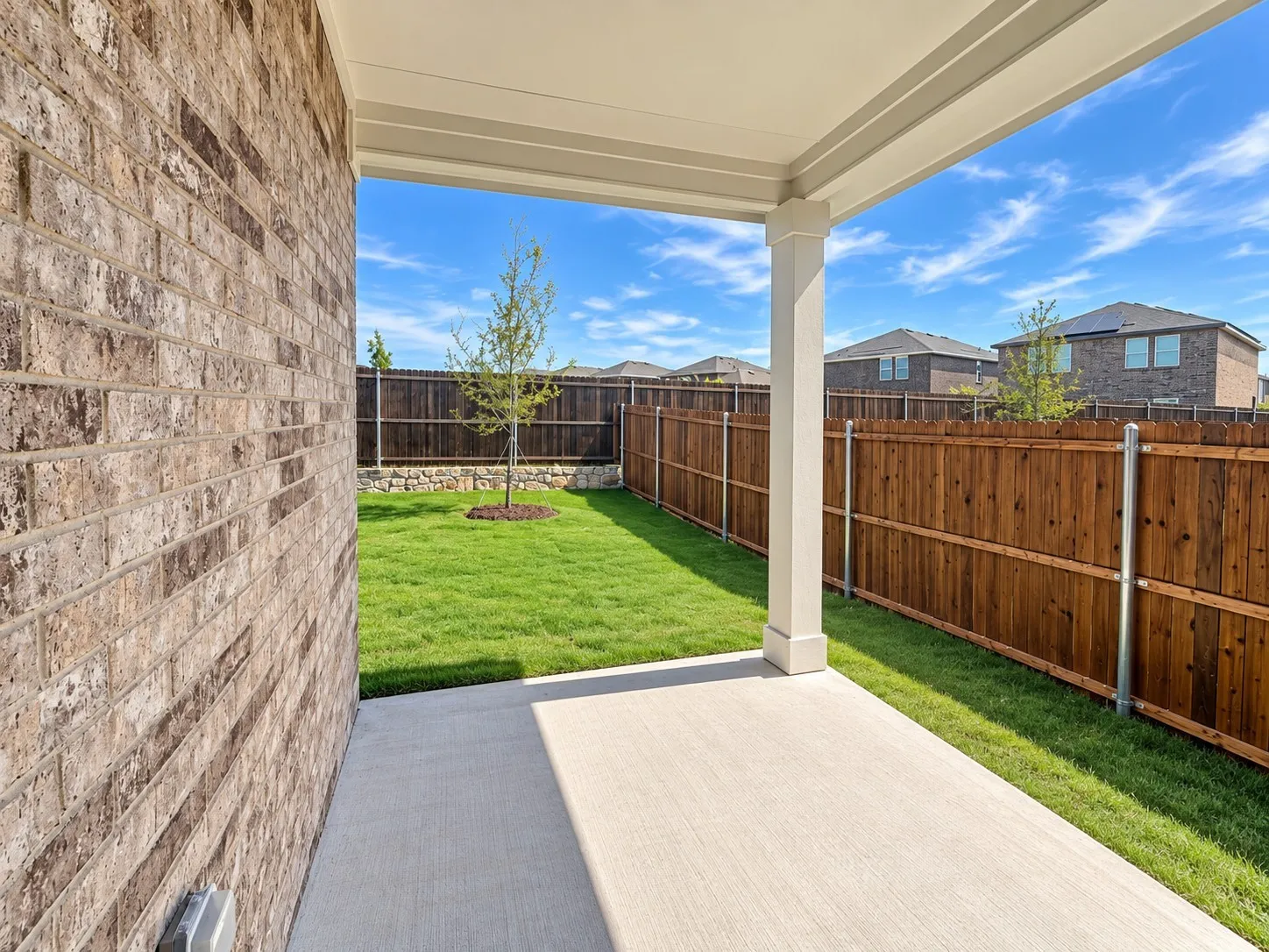 Covered patio with a concrete surface, brick exterior wall, and a wood-slat privacy fence