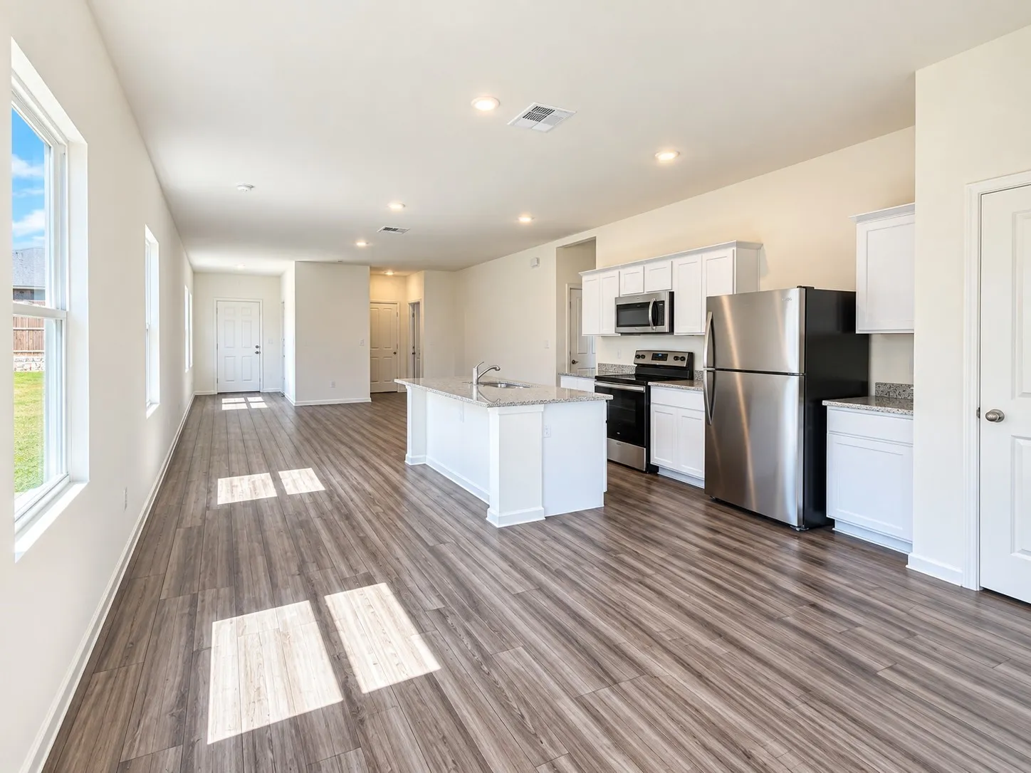 Spacious open-concept kitchen and dining area featuring white cabinetry, stainless steel appliances, wood-finish flooring throughout, recessed ceiling lighting, and an expansive island with prep space