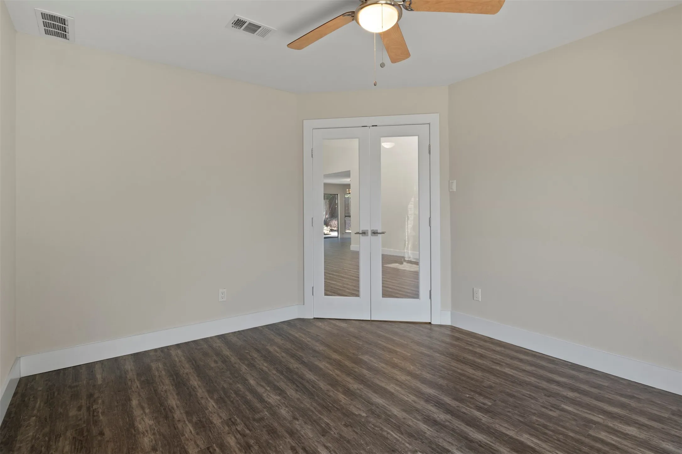 Wood-finish flooring, ceiling fan with integrated lighting, and double French doors with frosted glass panels