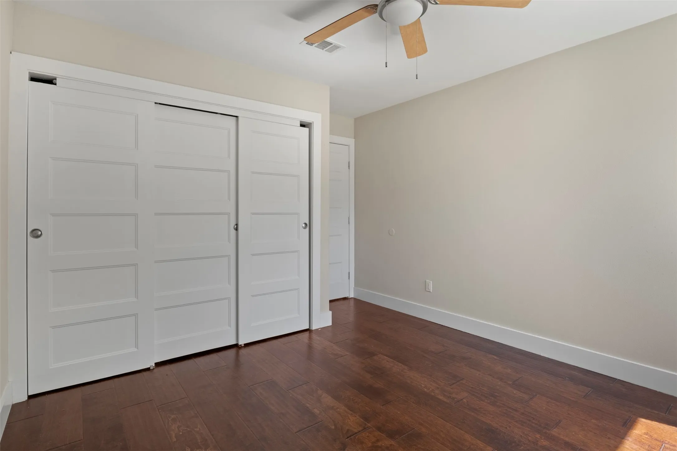 Wood-finish flooring, white sliding closet doors, ceiling fan with light fixture, and light-toned wall paint