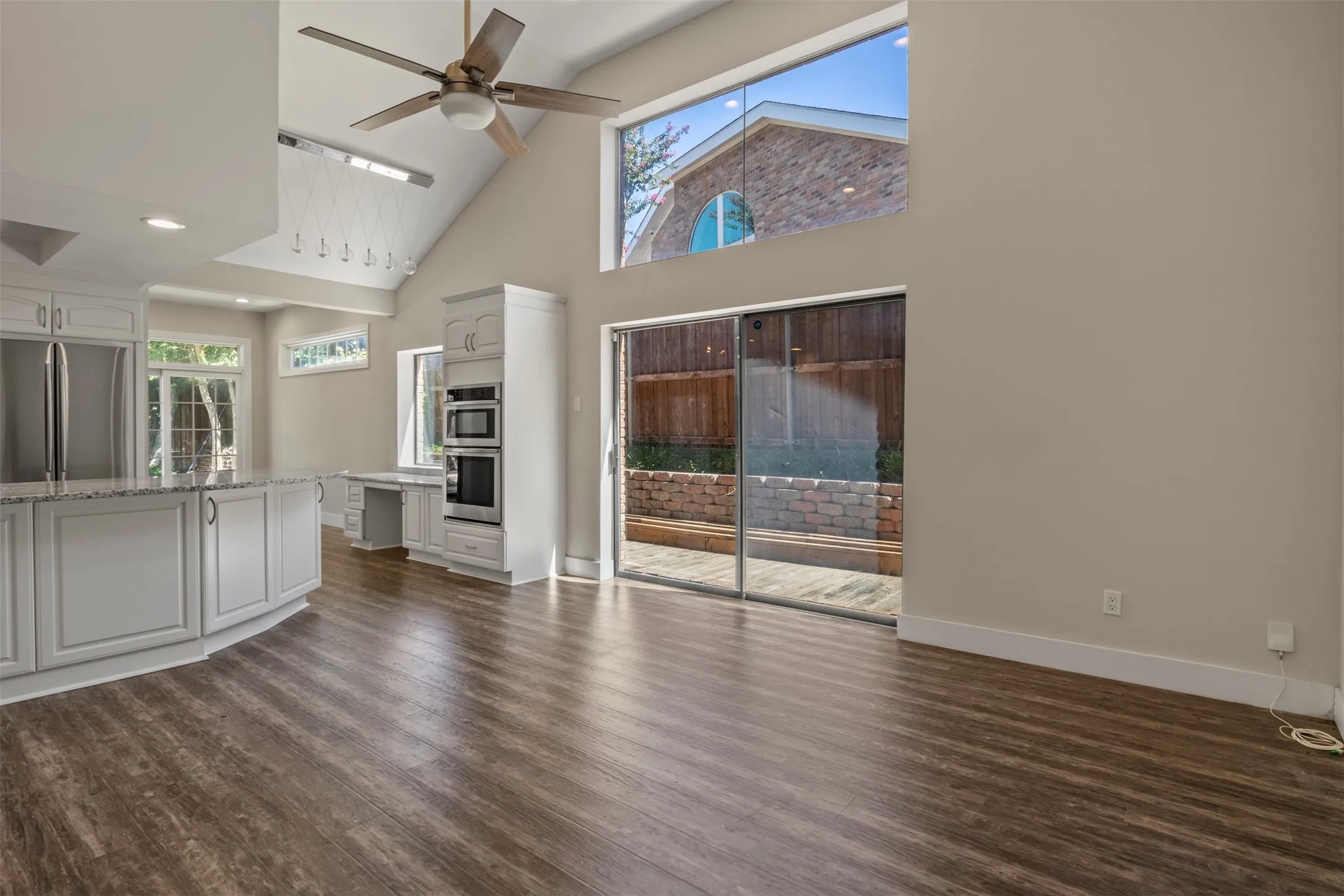 Vaulted ceiling with a ceiling fan, Luxury Vinyl Plank , white cabinetry with integrated appliances, sliding glass door, and large transom window