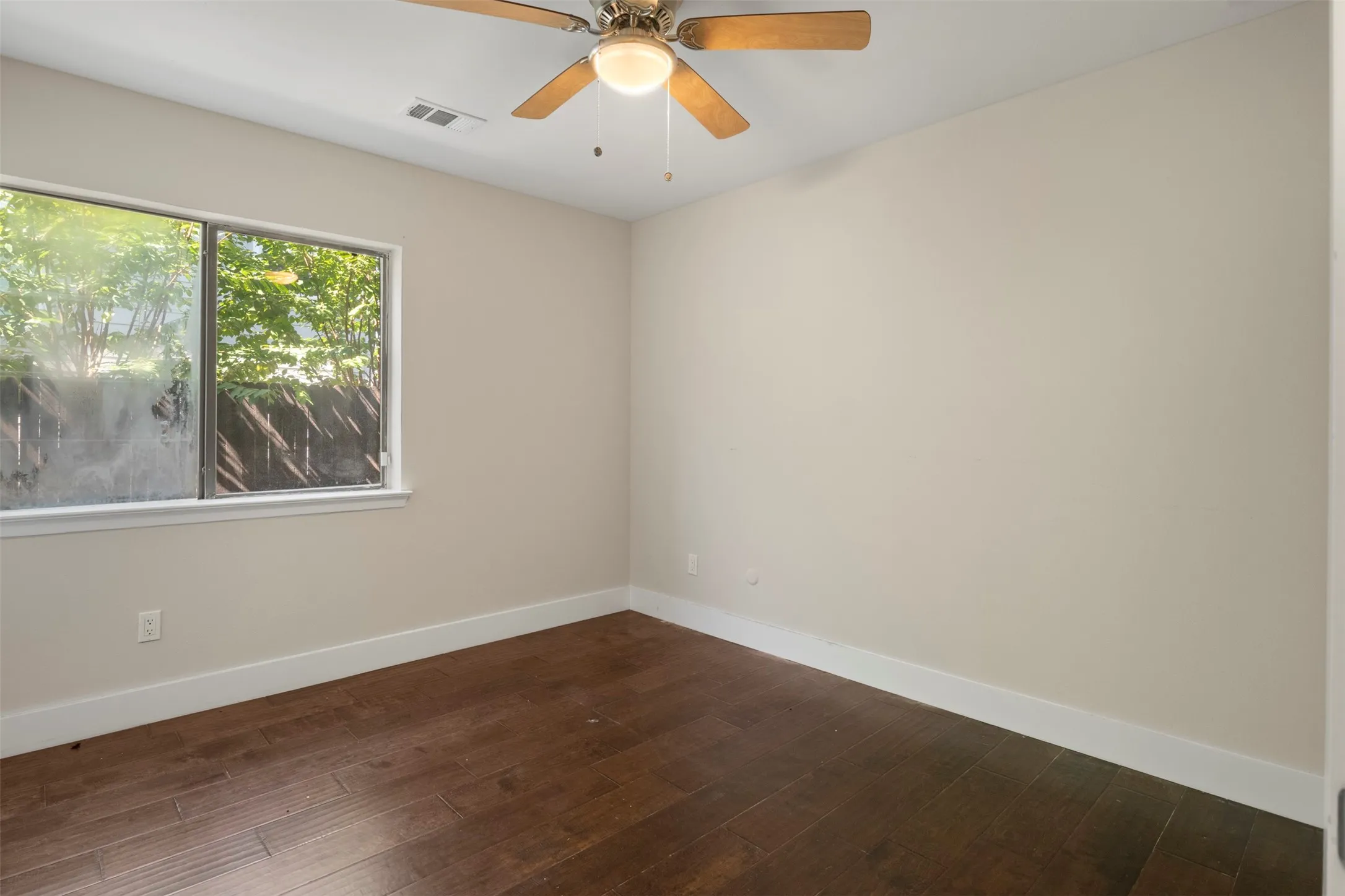 Hardwood-style flooring with white trim, a ceiling fan with integrated lighting, and a large window