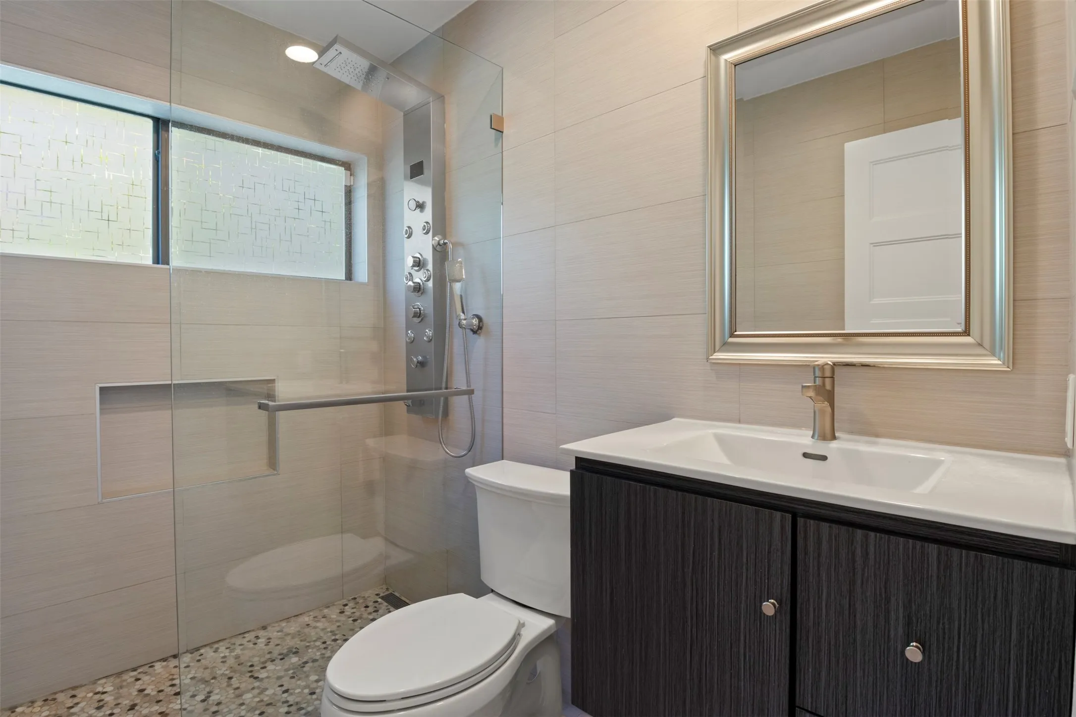 Glass-enclosed shower with a multi-function shower panel, pebble-finish floor, and recessed shelf
