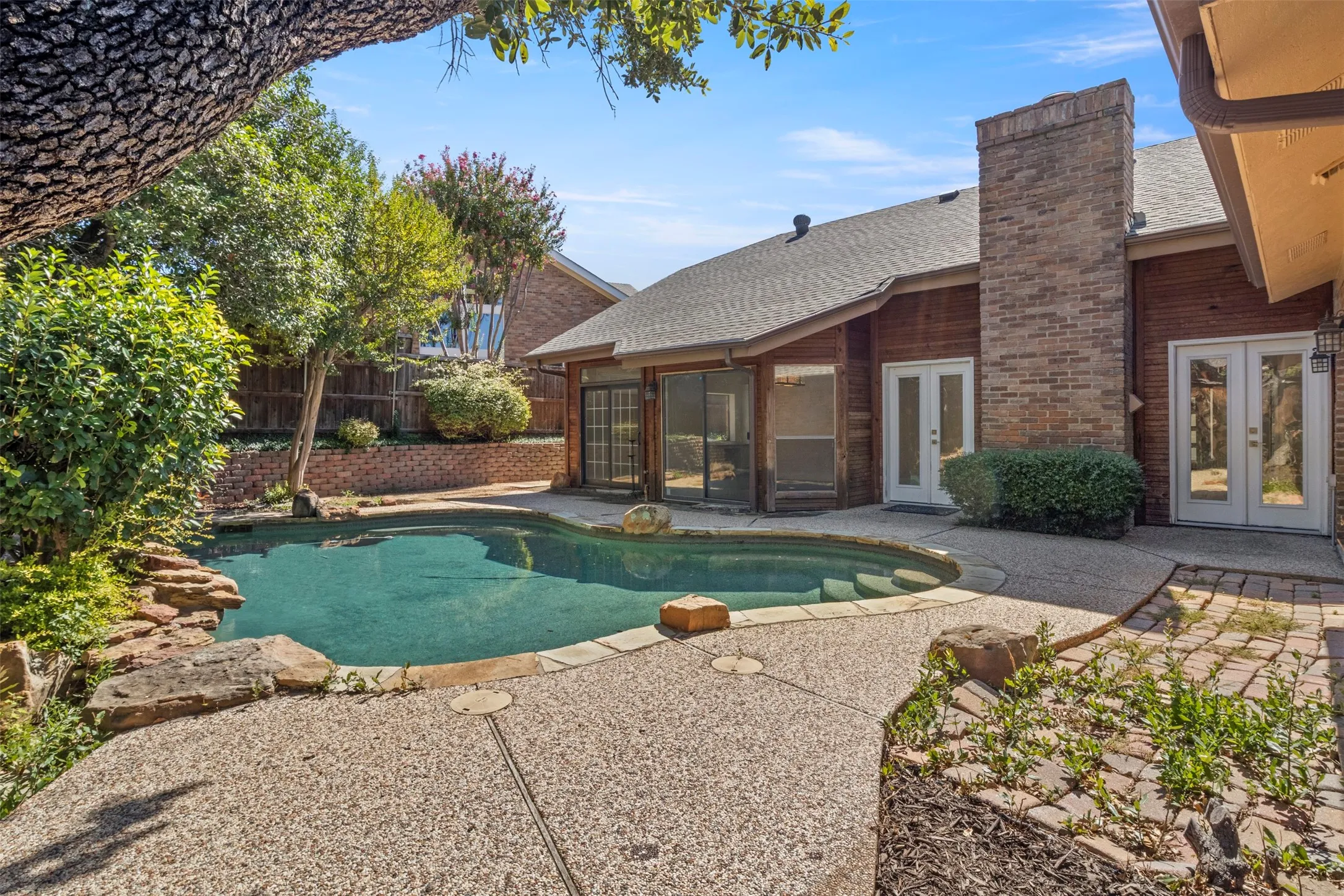 Expansive backyard featuring a freeform swimming pool, rock landscaping, and an exposed aggregate patio