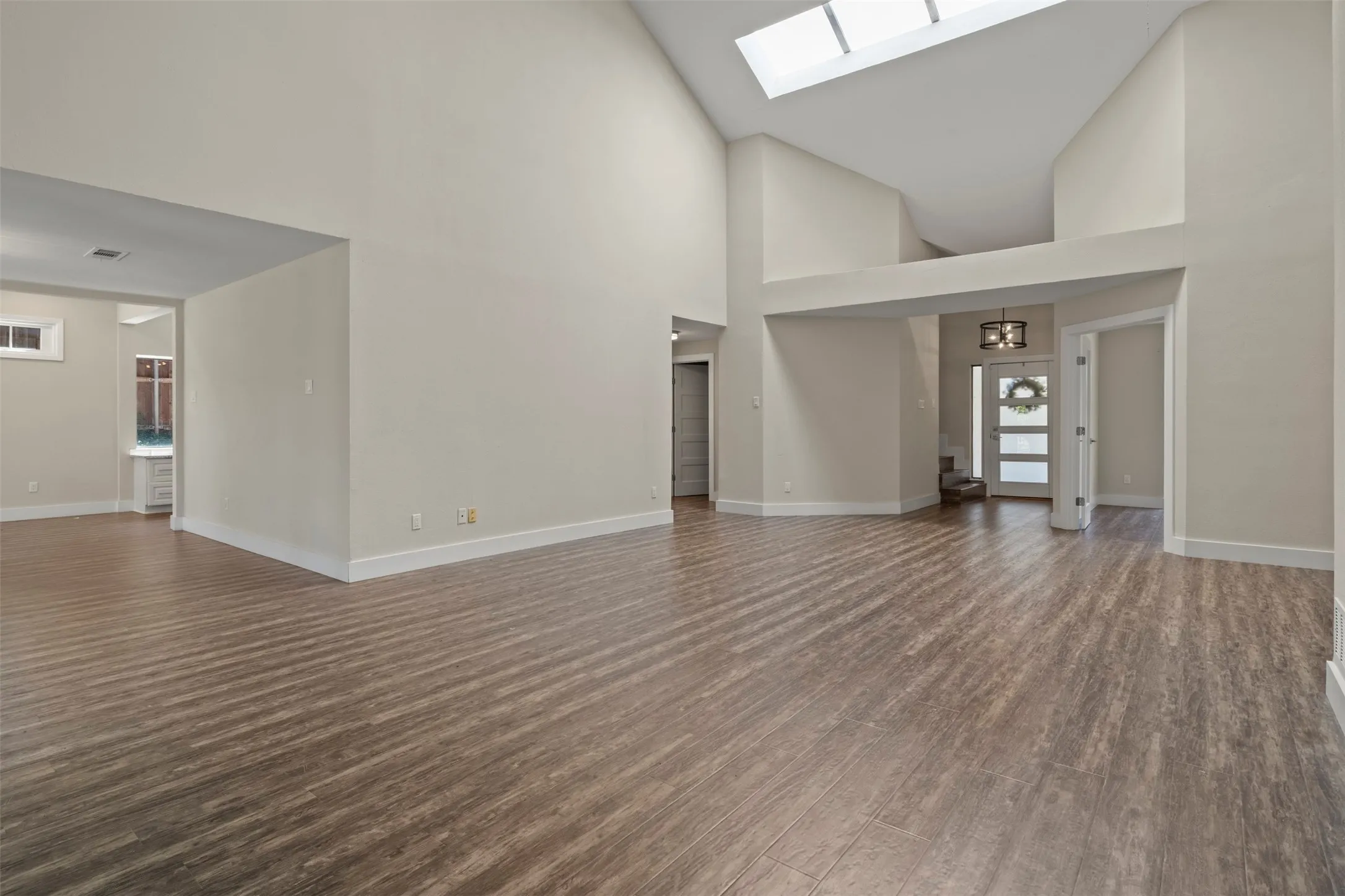 Vaulted ceilings, wood-finish flooring, an overhead skylight, and a white paneled front door with frosted glass inserts