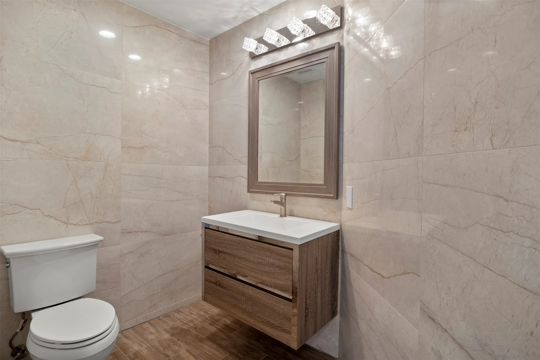 Floating wood-finish vanity with a white countertop and gold-tone faucet, complemented by a framed mirror