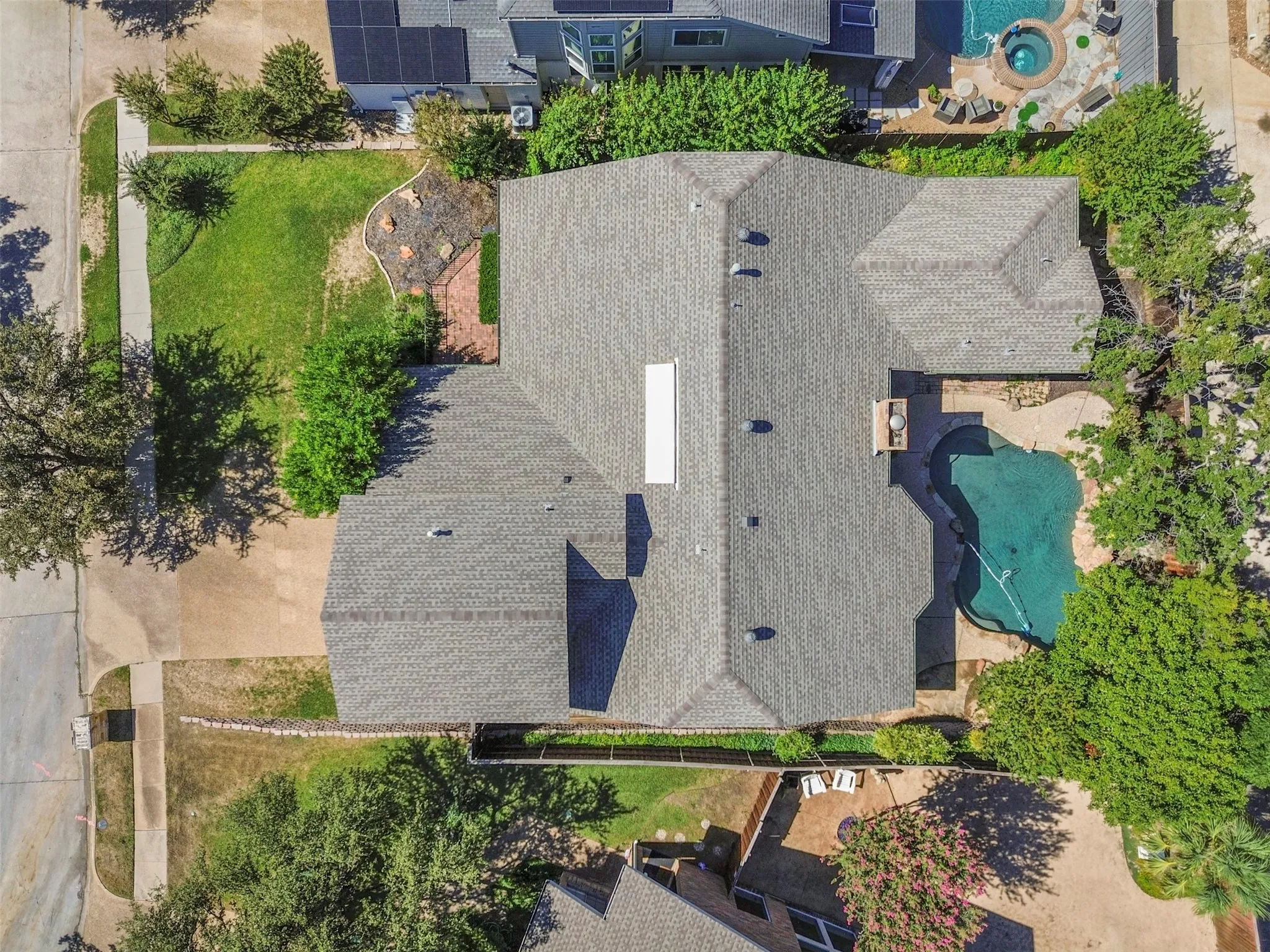 Aerial perspective showcasing a gabled roofline, a private swimming pool, mature perimeter landscaping, and a front yard with manicured lawn