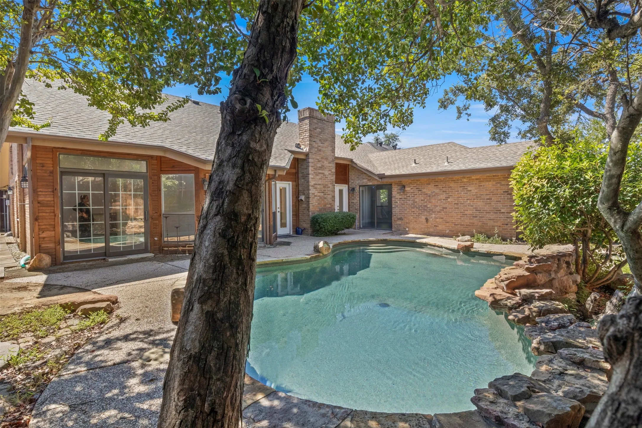 In-ground swimming pool with rock surround, extensive brick exterior, and multiple sliding glass doors