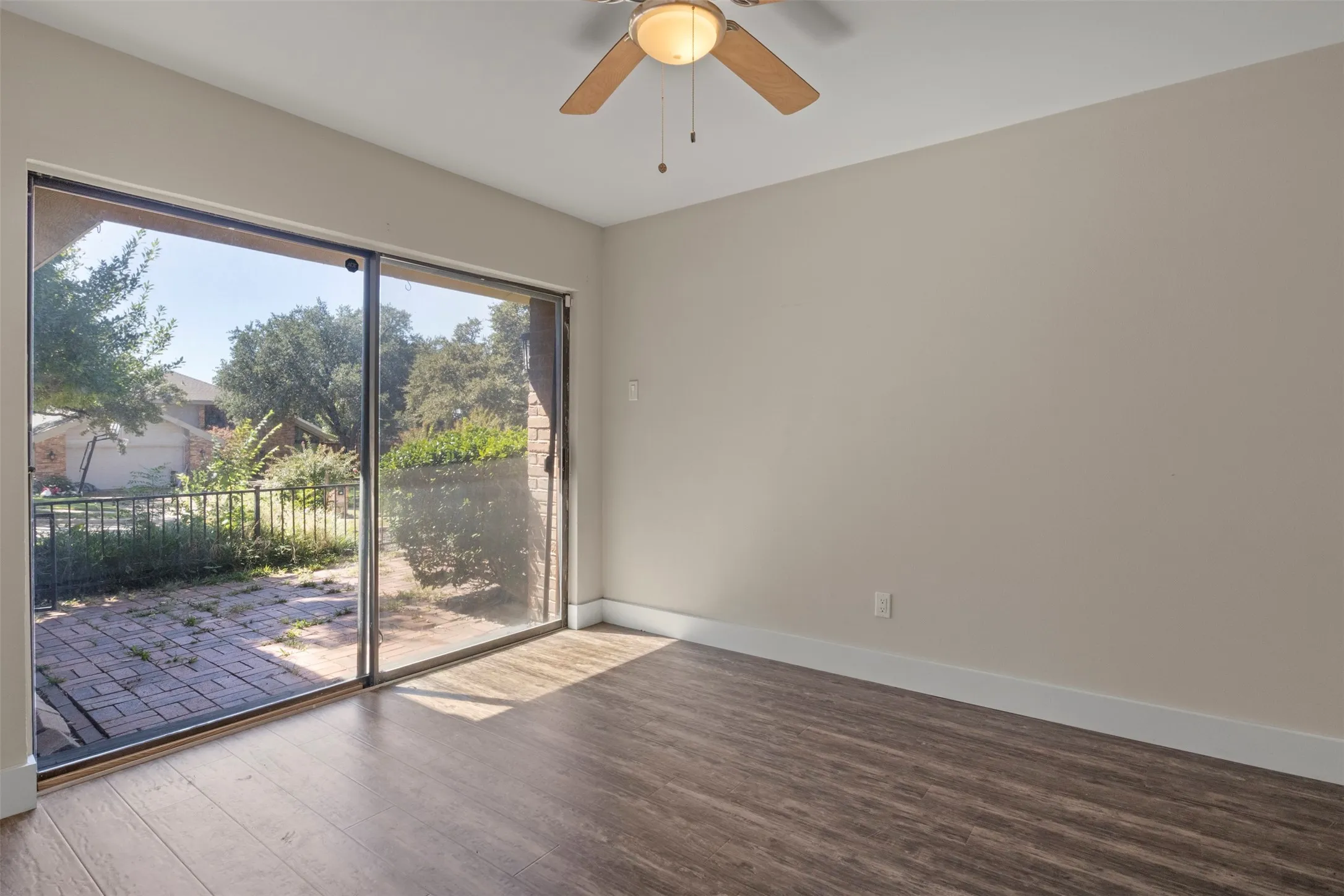 Wood-finish flooring, ceiling fan, sliding glass doors, and a paver patio
