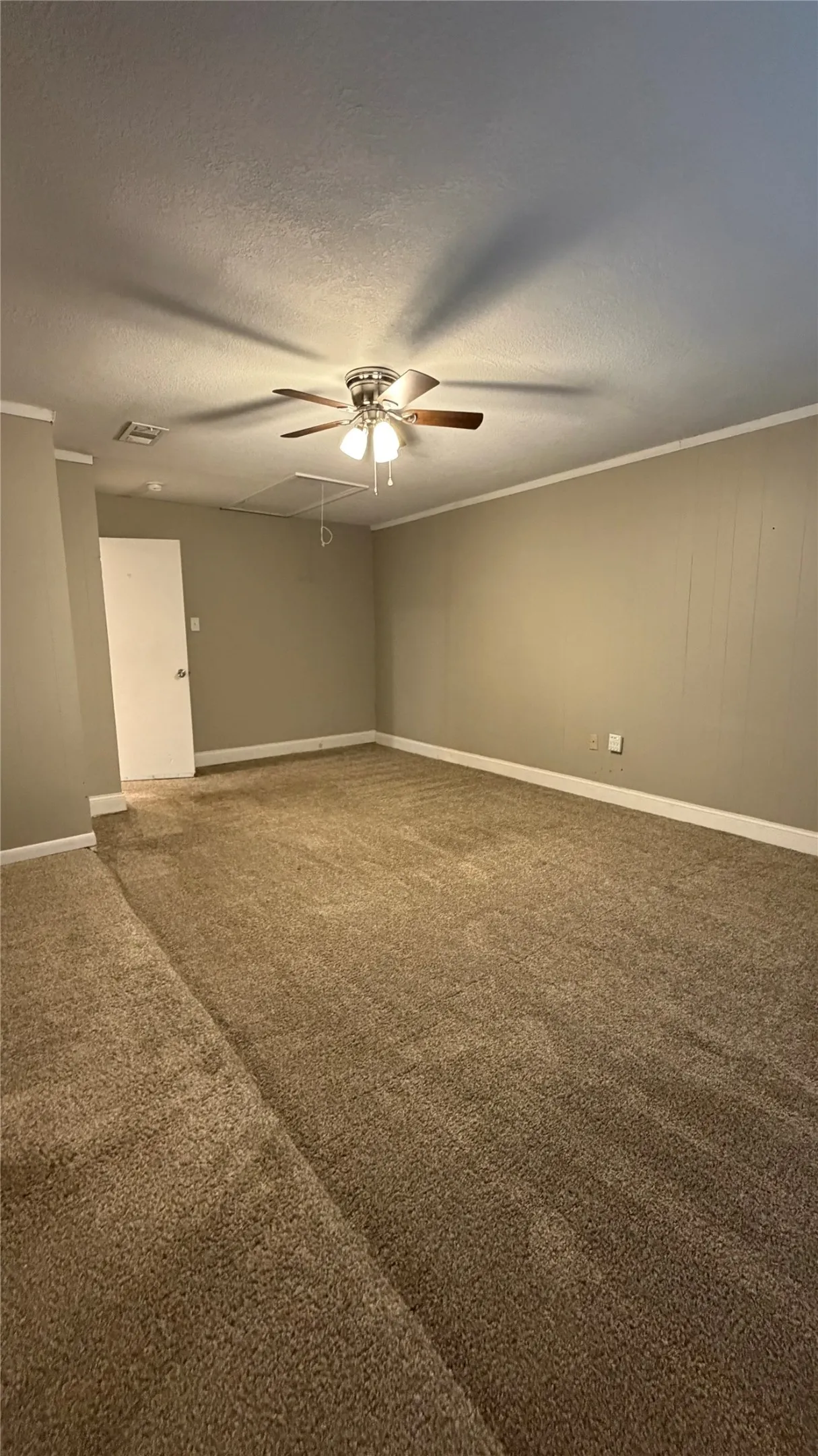 Plush carpet flooring, neutral-toned walls, ceiling-mounted fan with integrated lighting, white trim, and a white door with dark hardware