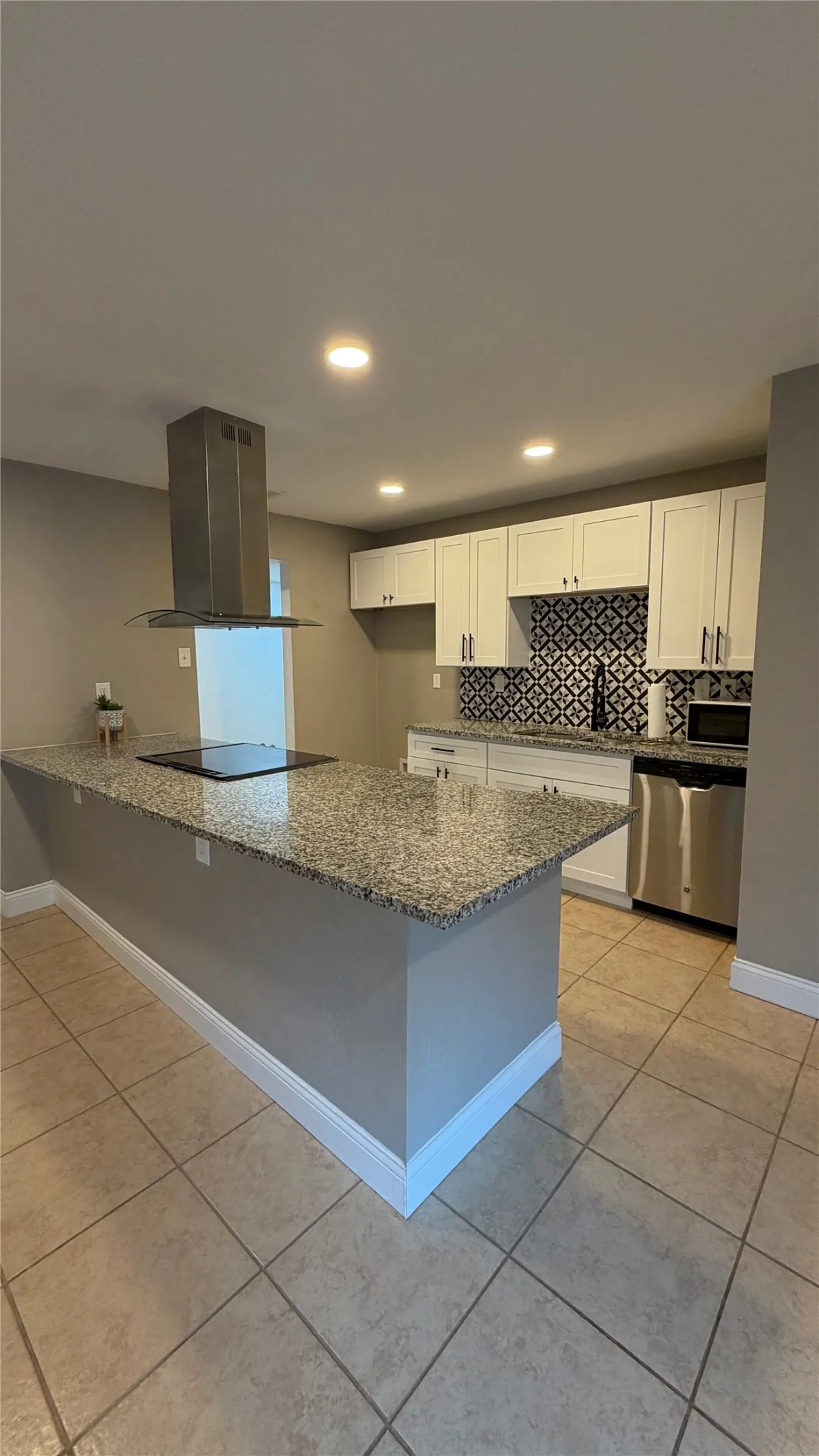 Kitchen featuring a central island with a built-in cooktop, granite countertops, stainless steel appliances, white cabinetry, and patterned tile backsplash