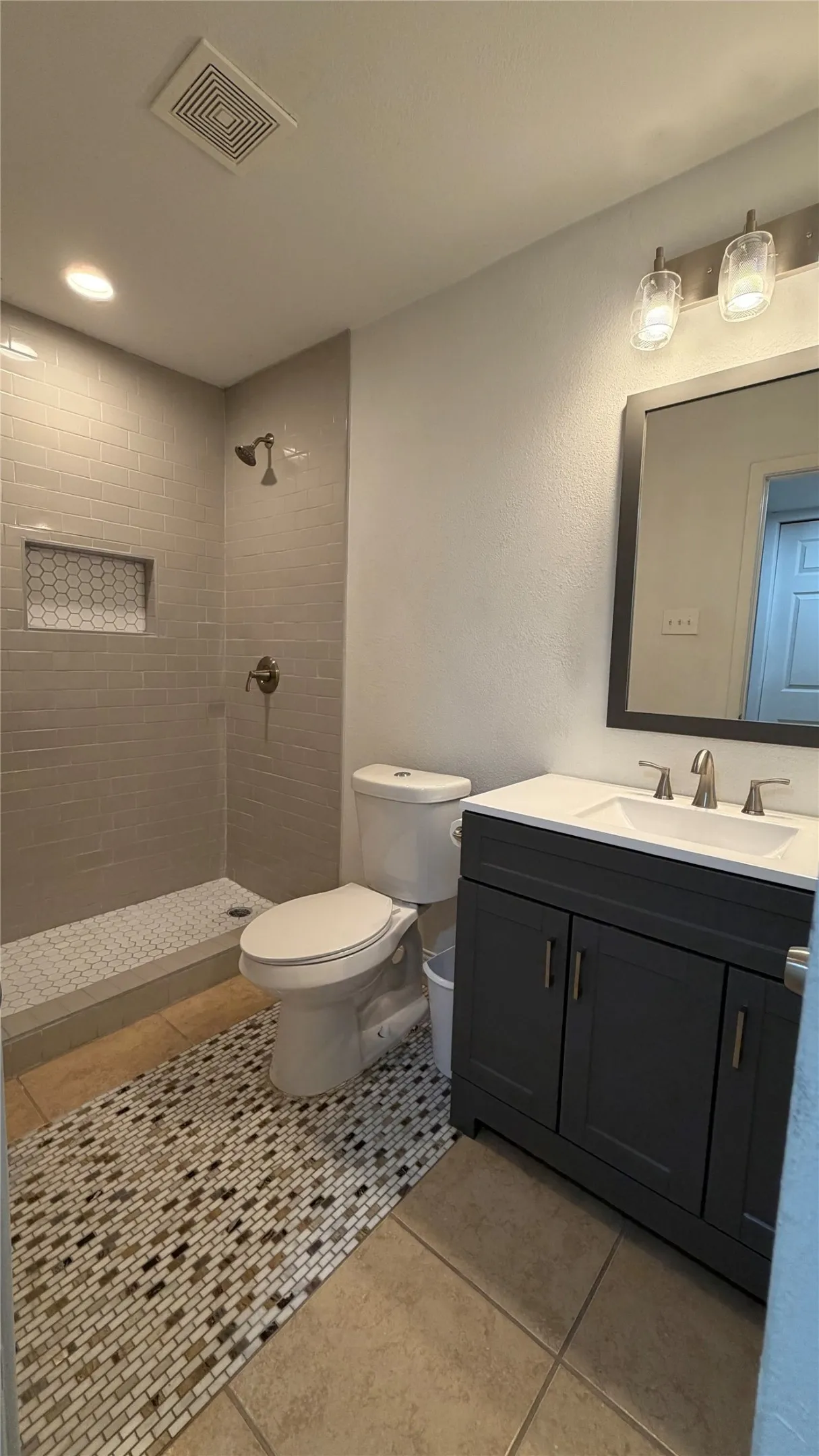 Walk-in shower with gray subway tile, mosaic shower pan, and recessed niche