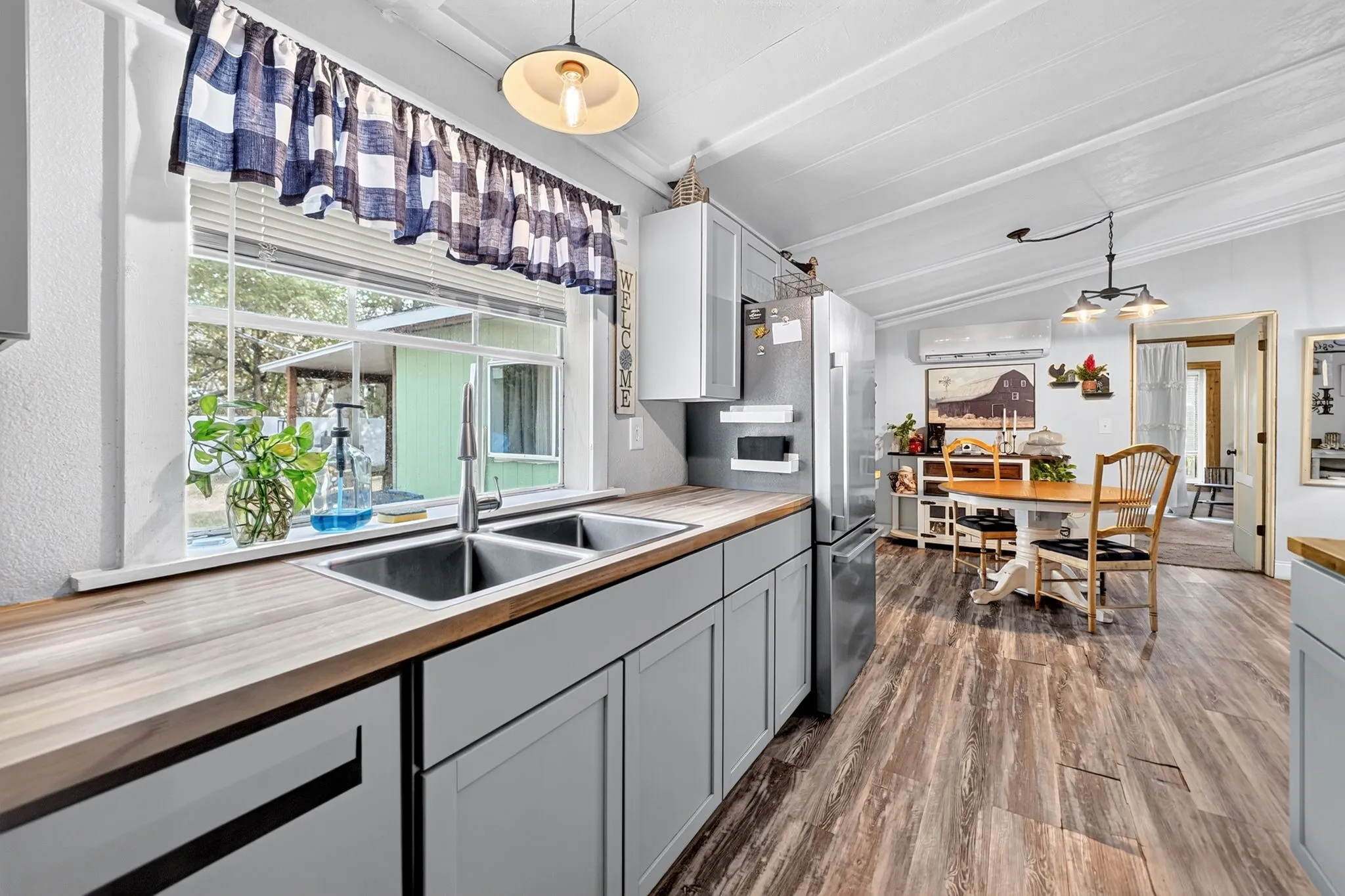 Kitchen featuring wood-finish countertops, stainless steel double basin sink with a gooseneck faucet, light gray cabinetry, and wood-finish flooring