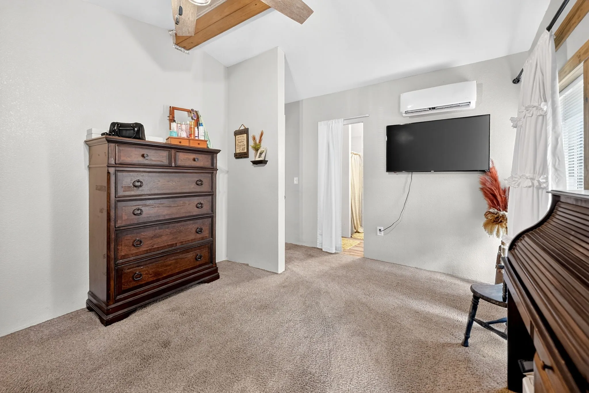 Carpeted flooring, vaulted ceiling with exposed wood beams, and a wall-mounted mini-split system