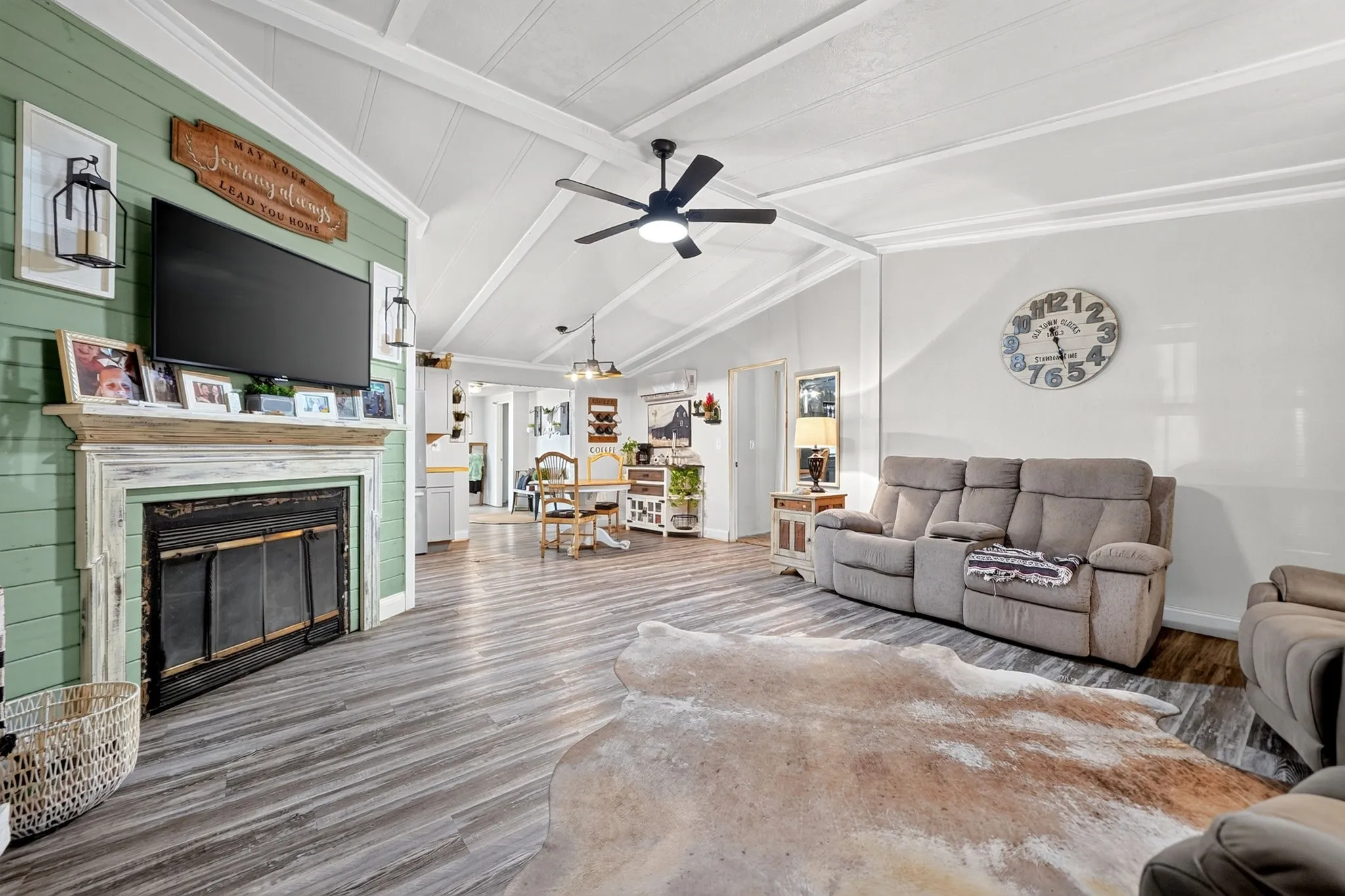 Living area featuring vaulted ceilings, wood-finish flooring, a decorative fireplace with a mantel, and a ceiling fan