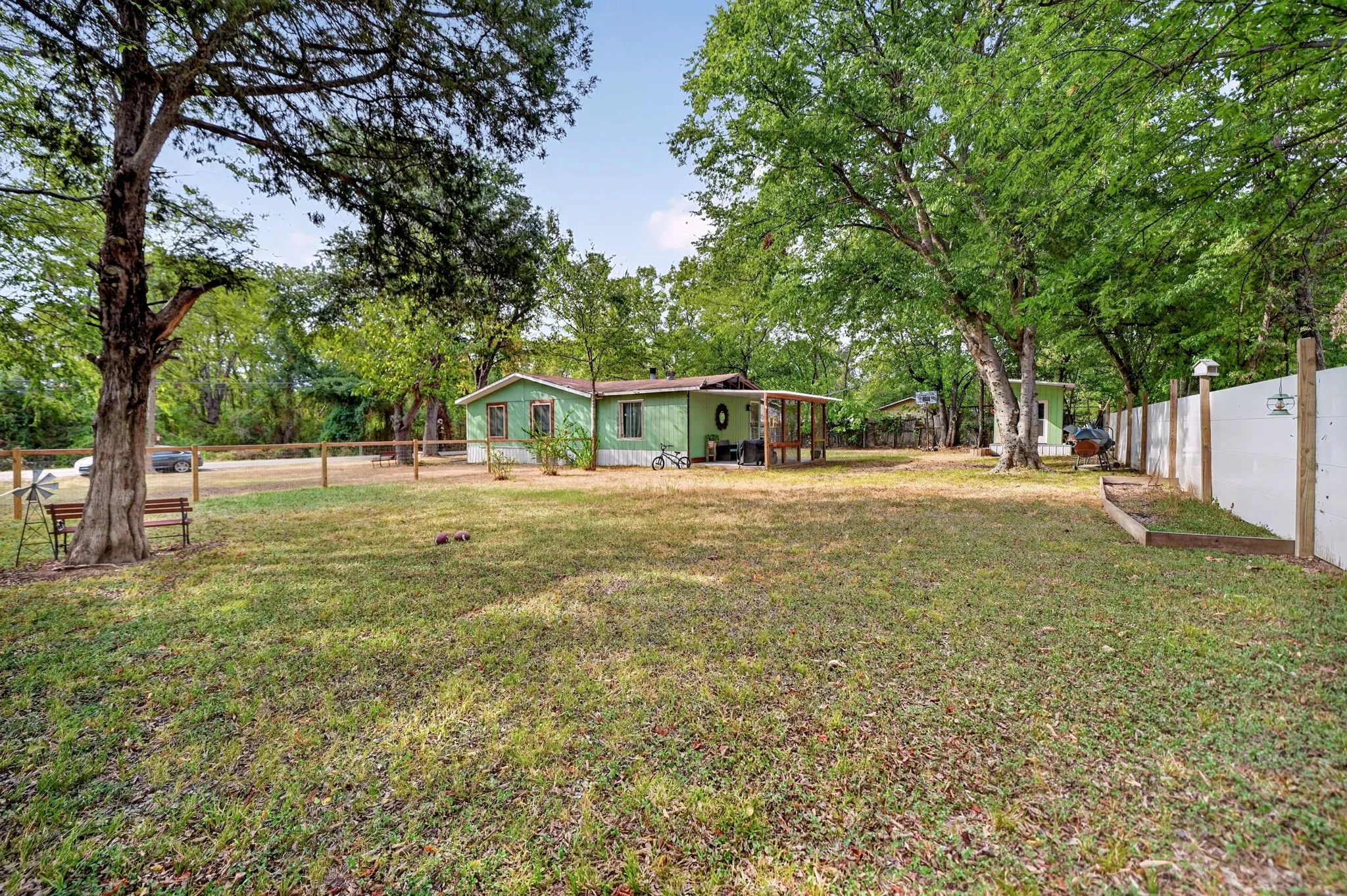 Expansive grassy yard framed by mature trees, featuring a white privacy fence and a wood fence