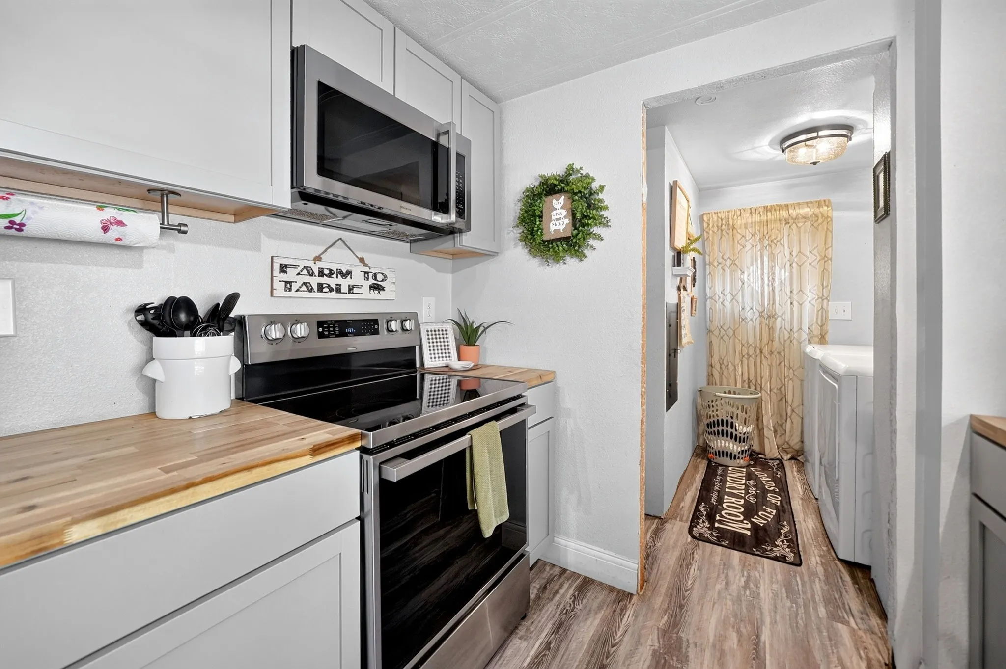 White upper and lower cabinetry, wood-finish countertops, stainless steel microwave, and a stainless steel range with a flat cooktop