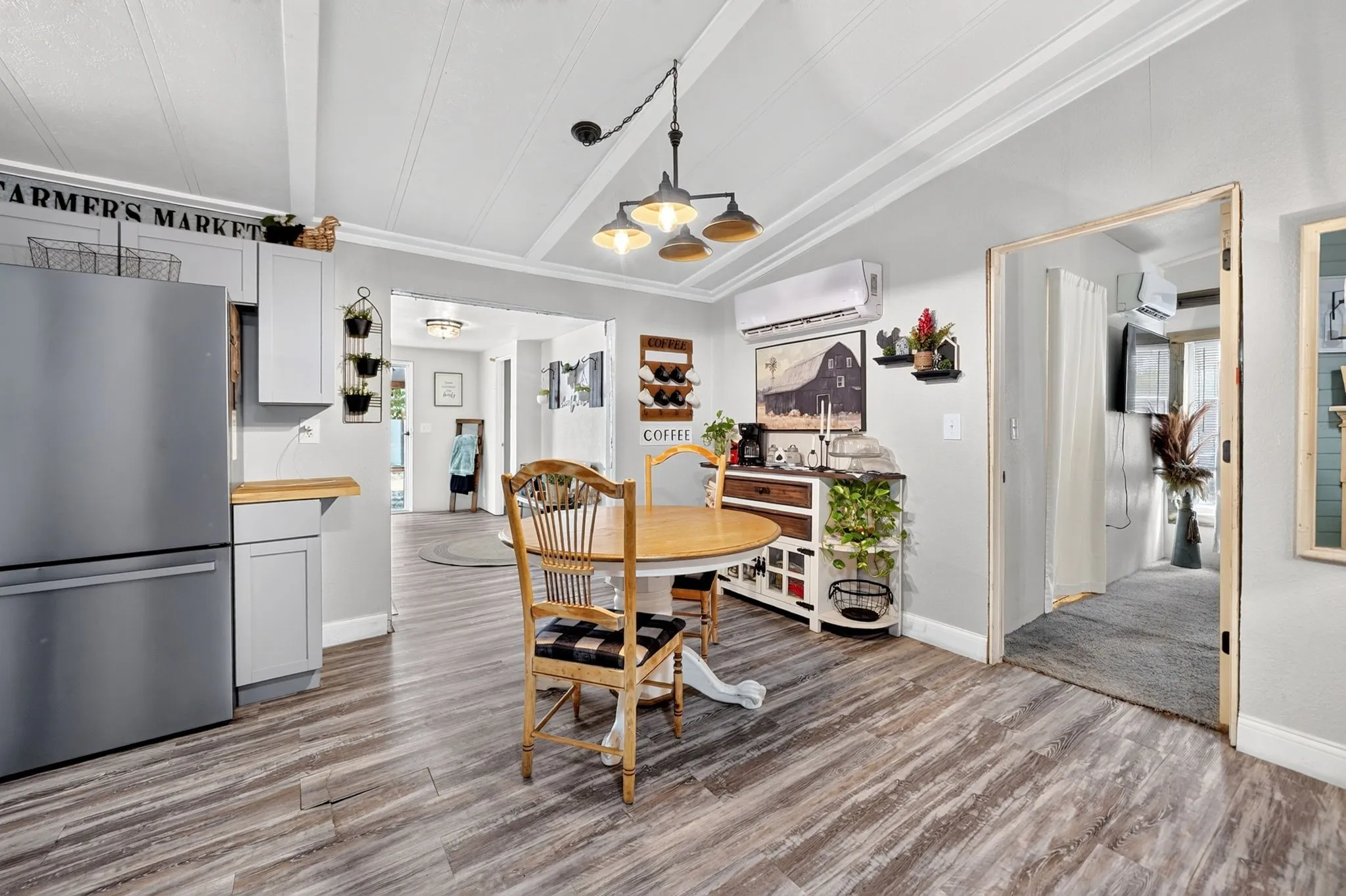 Vaulted ceiling with exposed beams, wood-finish flooring, light gray cabinetry, stainless steel refrigerator, and a suspended light fixture