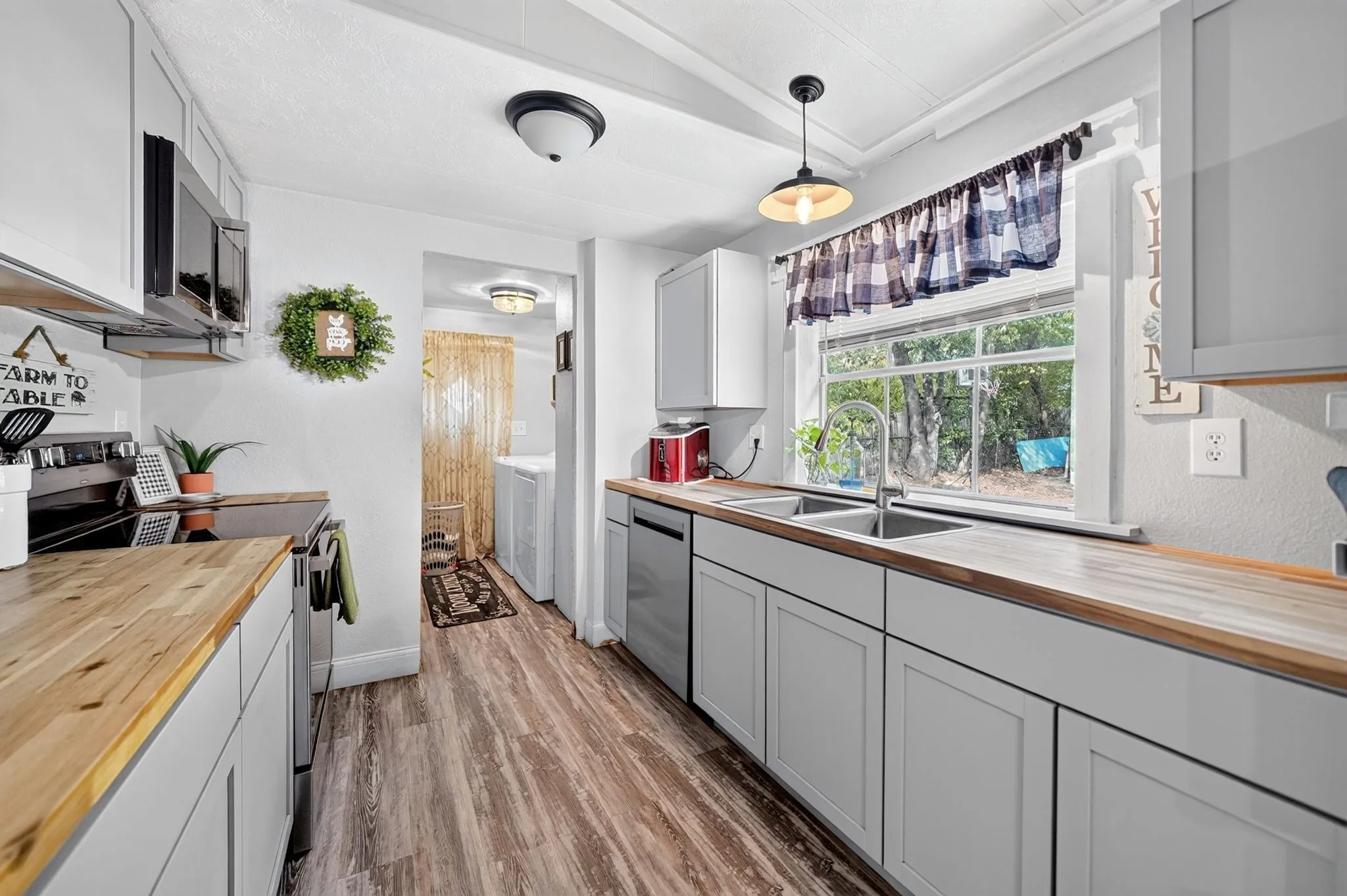 Galley kitchen featuring wood-finish countertops, stainless steel appliances, white cabinetry, a double basin sink, and wood-finish flooring