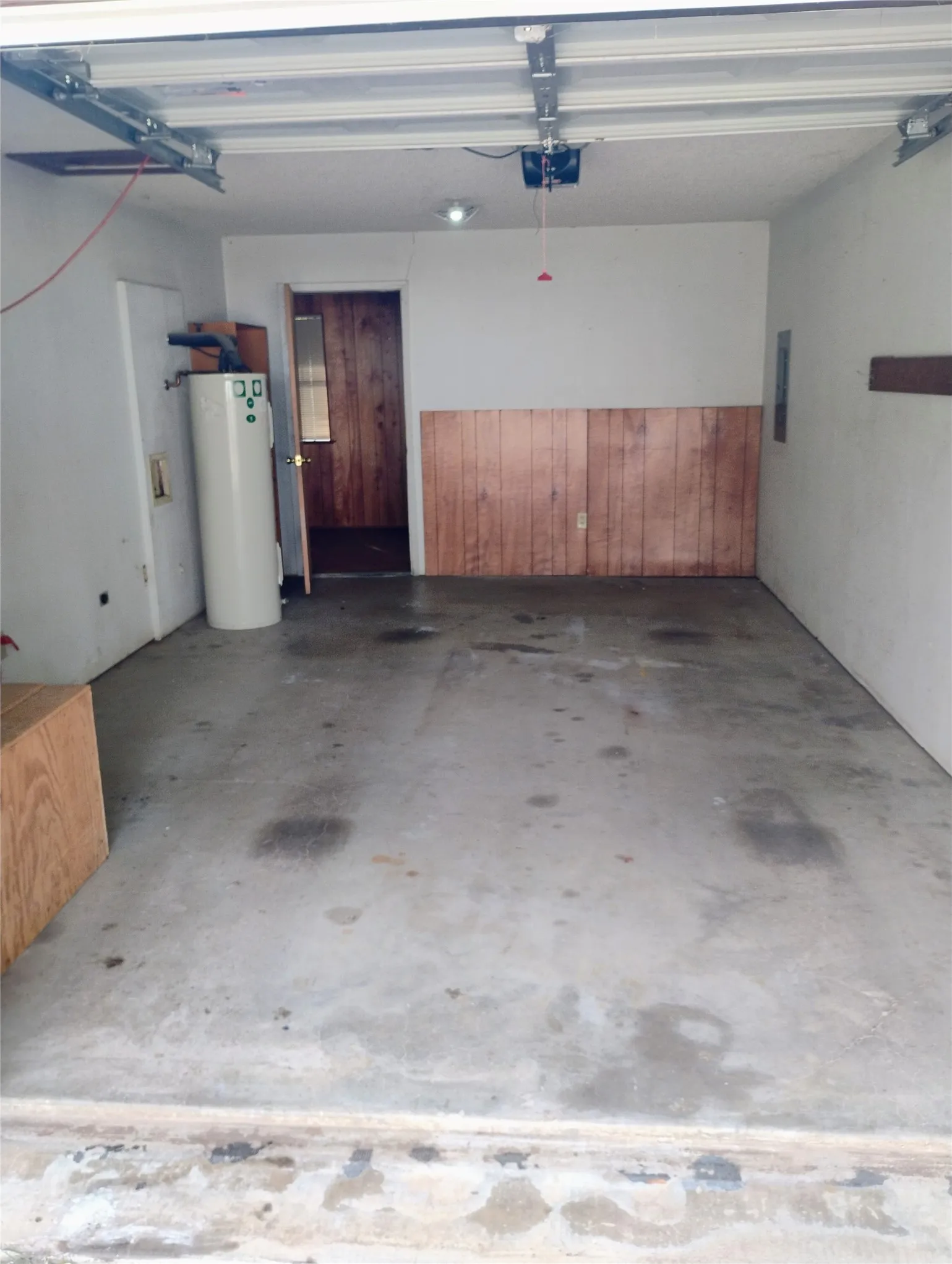 Concrete flooring in a single-car garage with a water heater and a wood-paneled wall accent