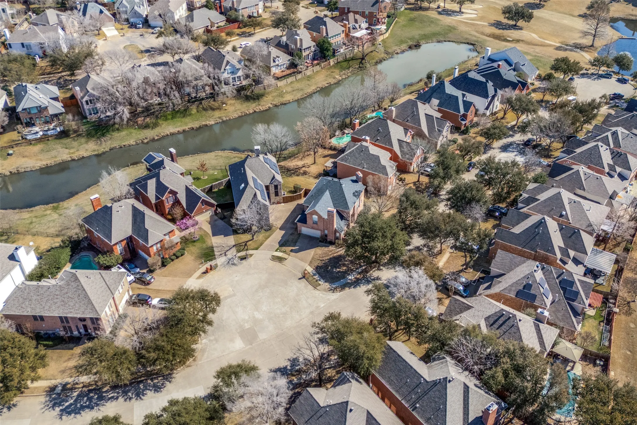 Aerial perspective showcasing a residential community with mature landscaping, multiple properties with red brick exteriors, and a winding waterway