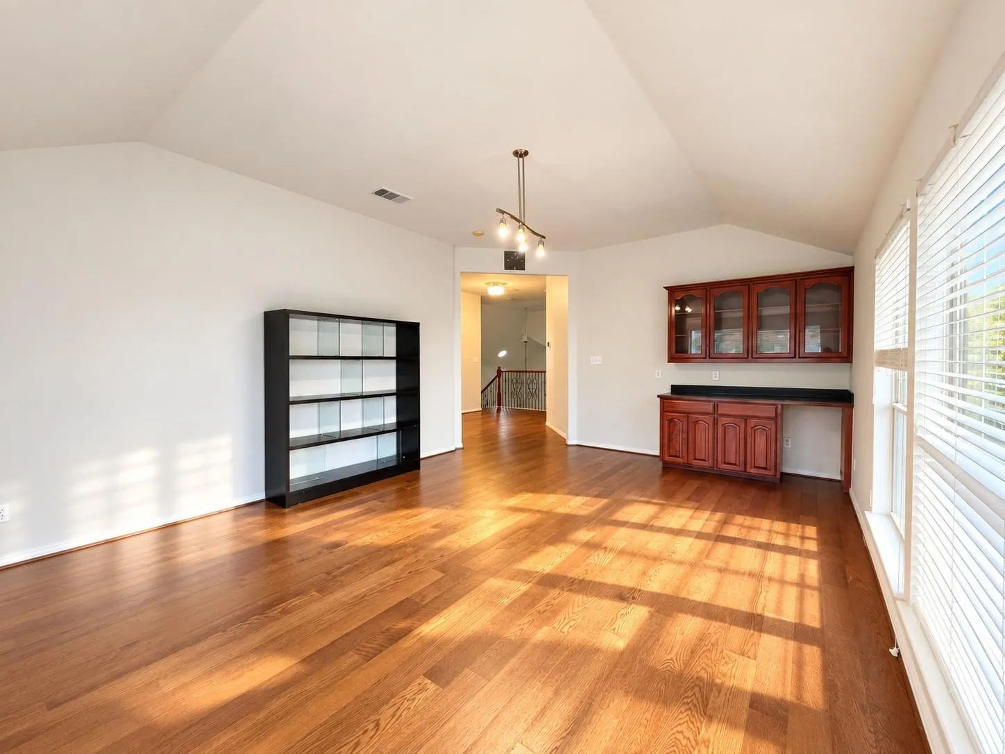 Vaulted ceiling, wood-finish flooring, track lighting, built-in cabinetry with glass-front uppers, and large windows with blinds