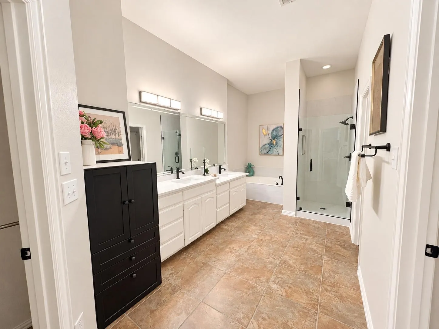 Spa-inspired primary bathroom featuring dual vanities with white cabinetry, black hardware accents, and quartz countertops