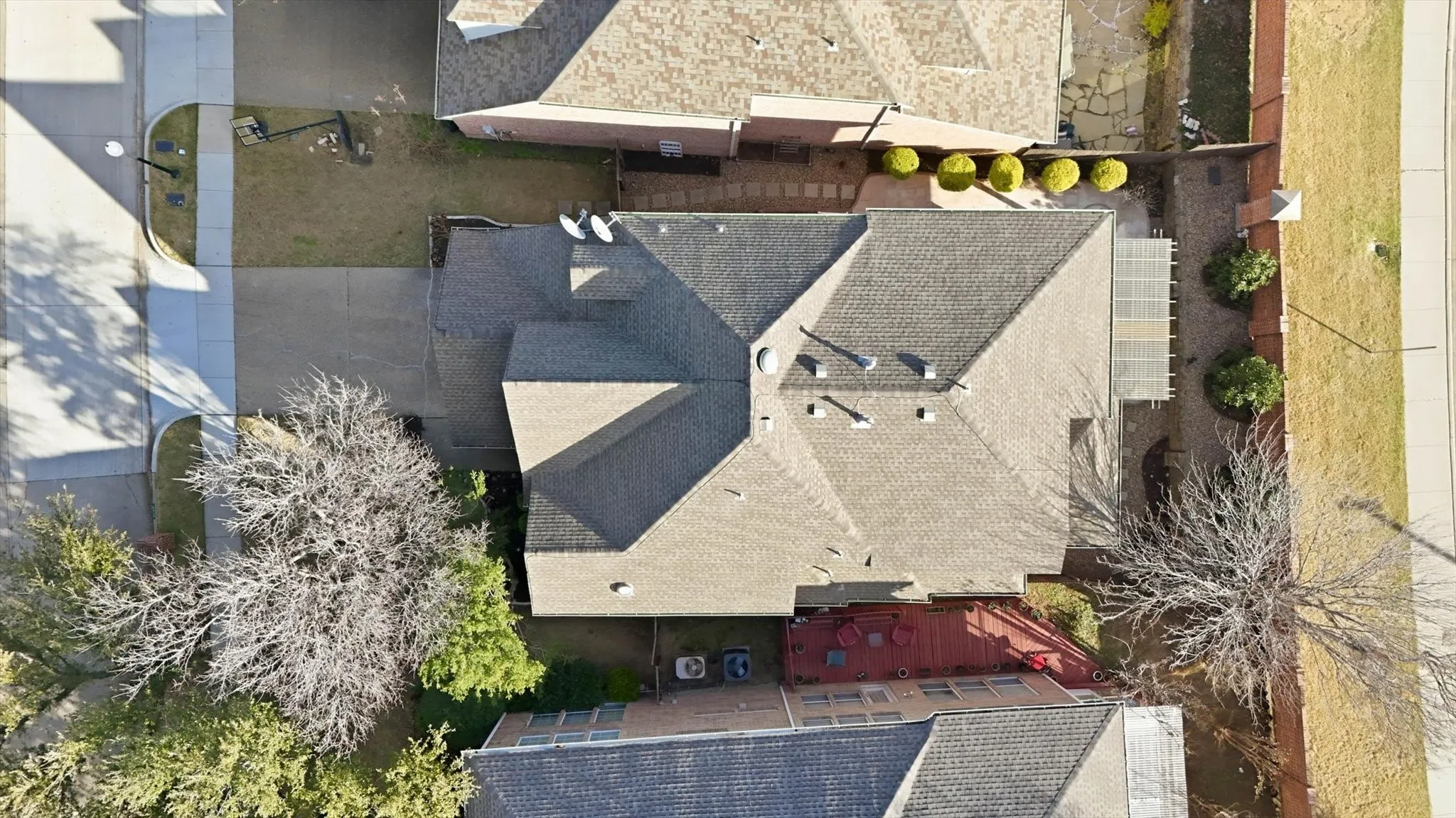 Pitched roof with shingles, paved driveway, landscaped front yard, and a covered patio area
