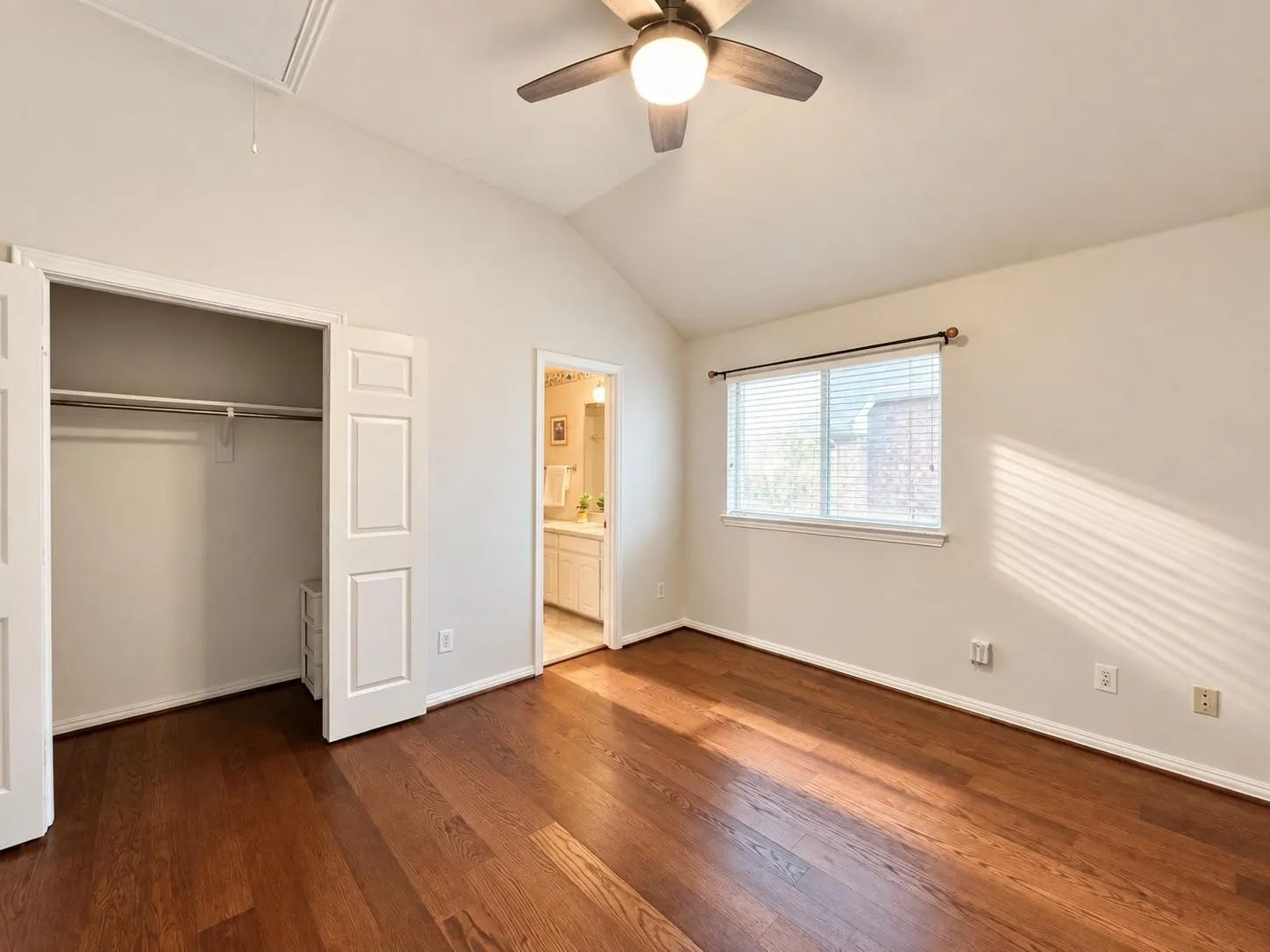 Vaulted ceiling with an attached ceiling fan, hardwood flooring, and a double-door closet