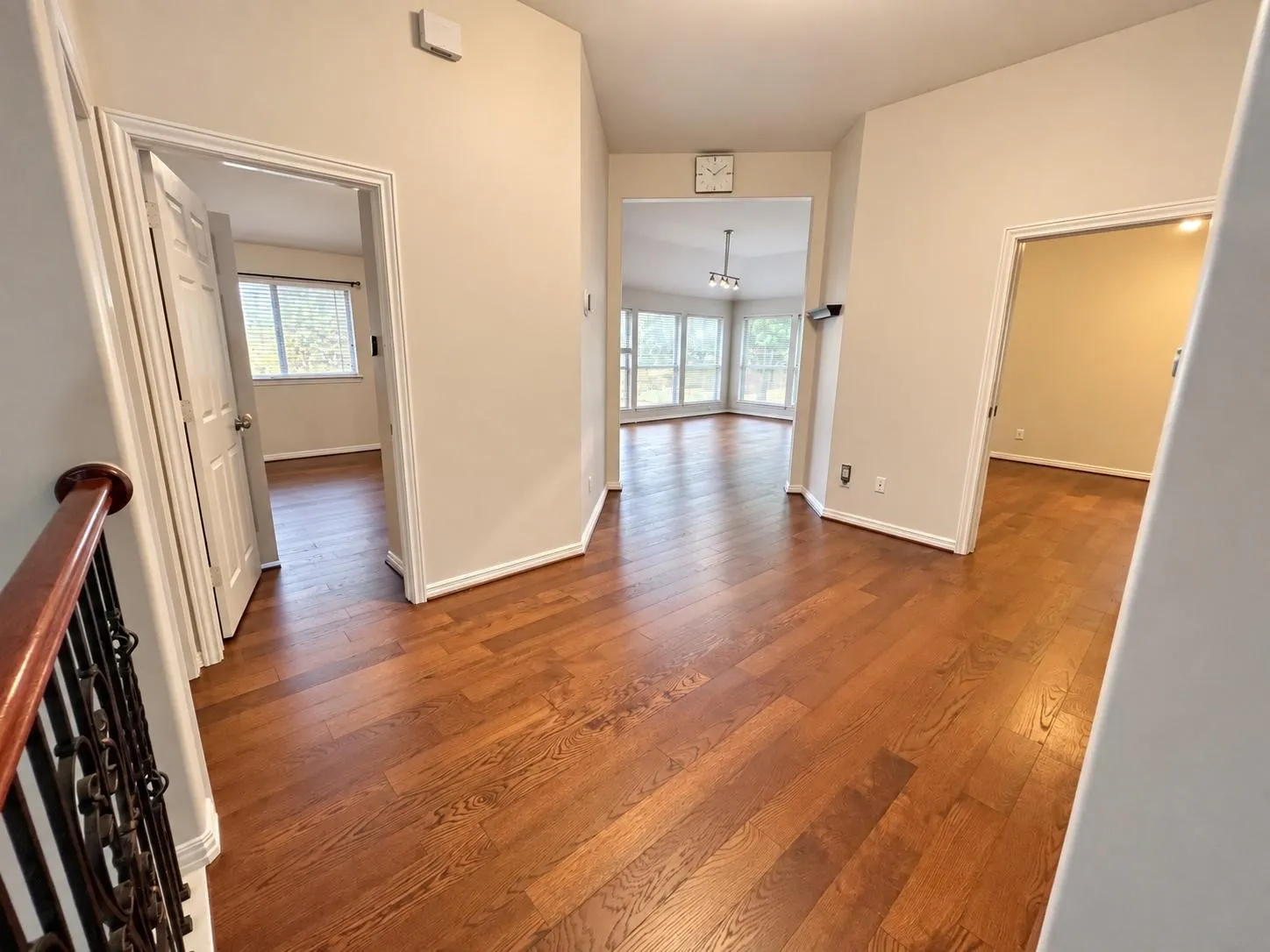 Hardwood flooring throughout, multiple doorways leading to separate rooms, bright windows with natural light, and a wrought iron and wood-finish railing