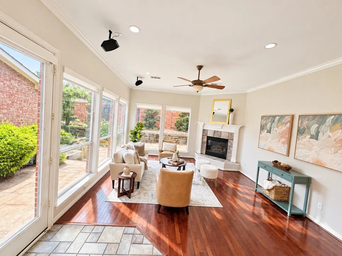 Rich wood-finish flooring, stone-surround fireplace, ceiling fan, and extensive window system overlooking an exterior patio