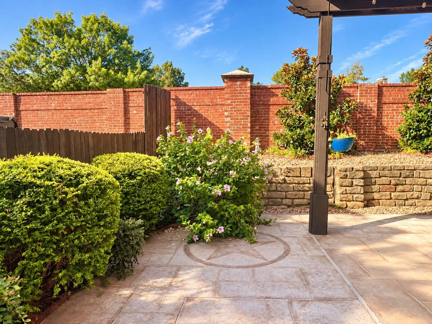 Paved patio featuring an inlaid star design, a dark wood-finish pergola, and mature landscaping