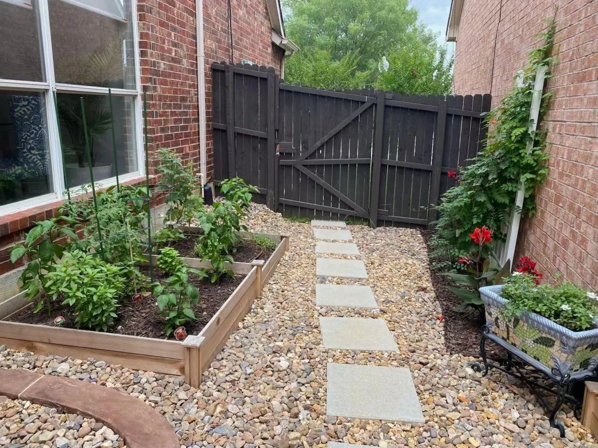Brick exterior with garden beds, a gravel path, stepping stones, and a dark wood privacy fence