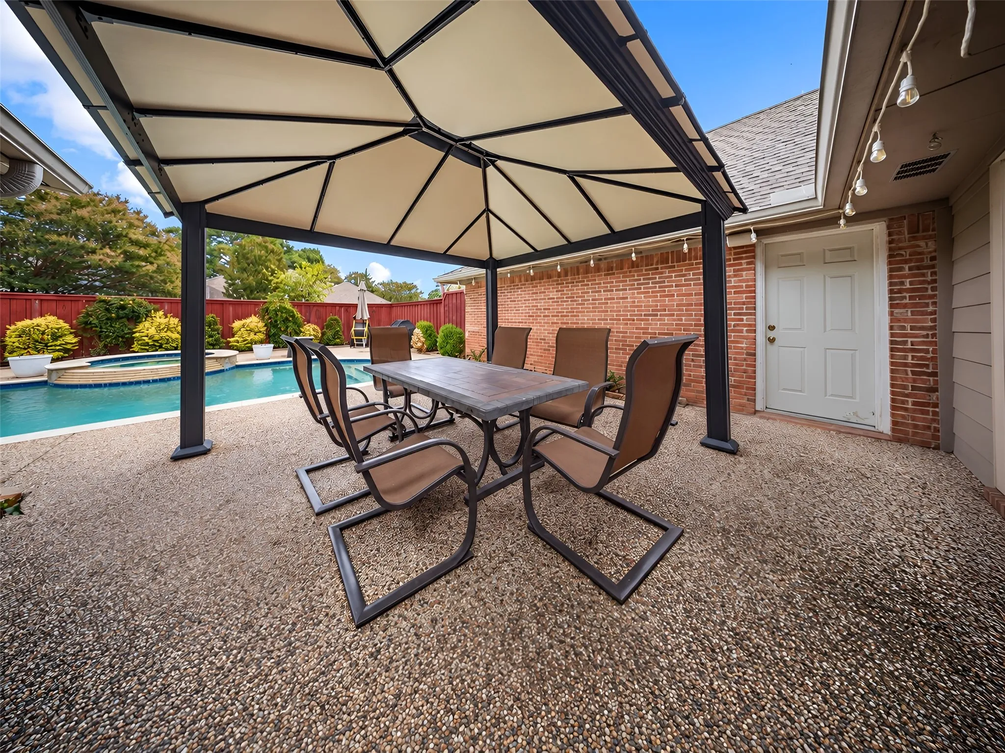 Outdoor living area featuring a covered patio, exposed aggregate concrete flooring, an in-ground swimming pool, and a brick exterior