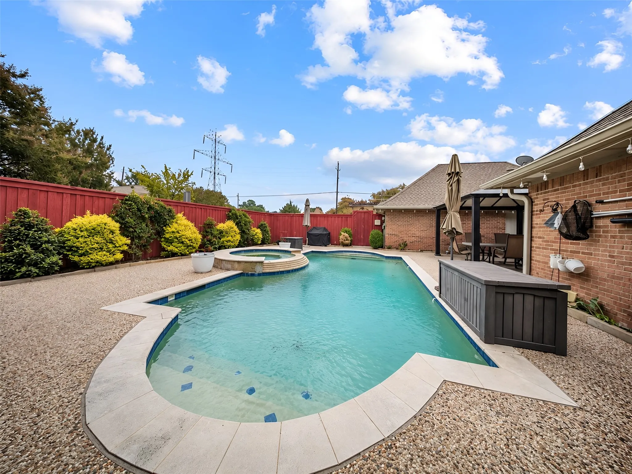 Expansive backyard featuring a large swimming pool, integrated spa, surrounding aggregate rock hardscaping, and a covered patio area