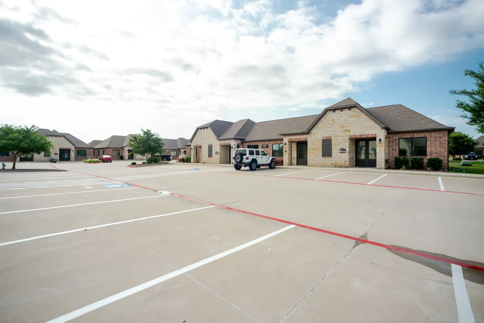 Brick and stone exterior, gabled rooflines, dark-framed windows, and a concrete parking area
