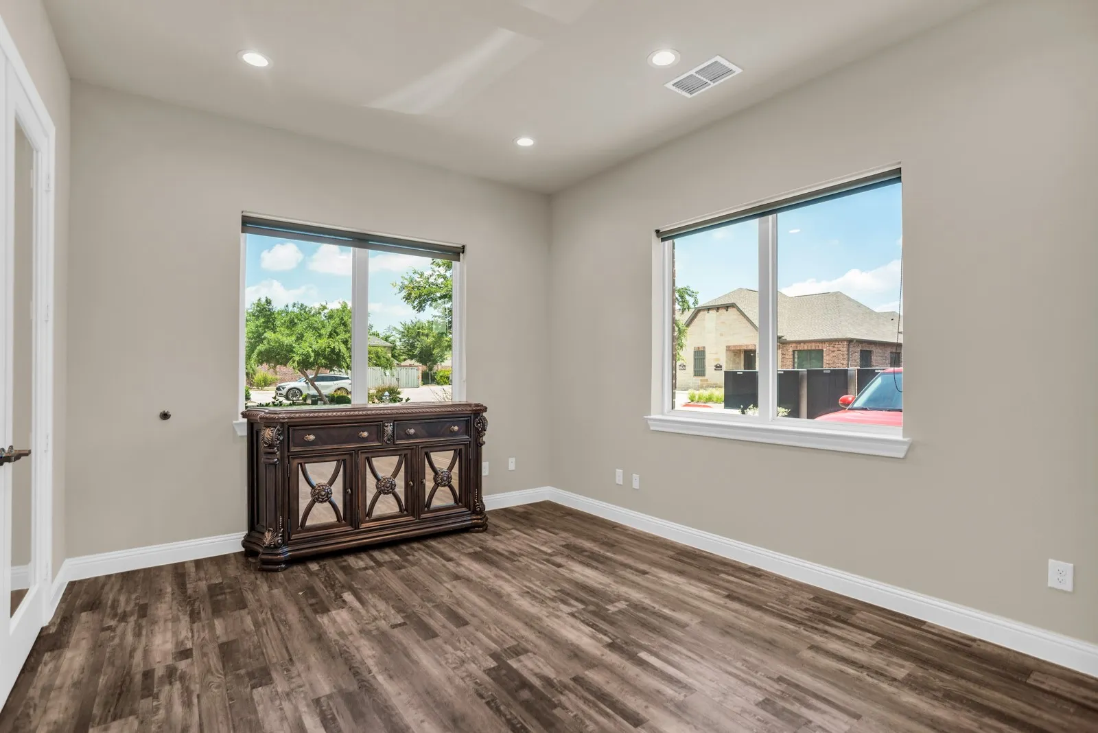 Recessed ceiling lighting, wood-finish flooring, two large windows, white trim, and a paneled door with hardware