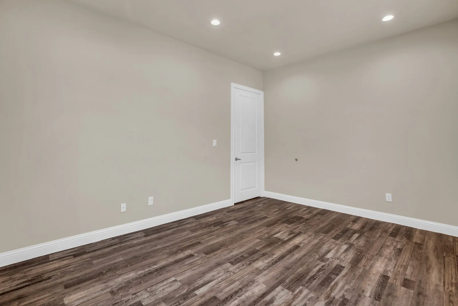 Wood-finish flooring, recessed lighting, neutral wall tones, and a paneled door with contemporary hardware