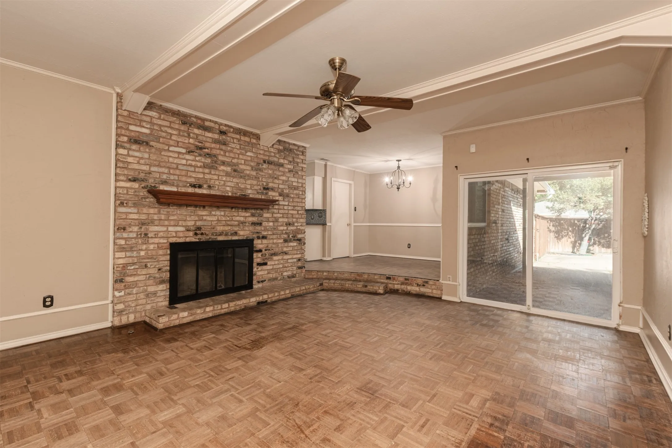Brick fireplace with wood mantel, parquet flooring, beamed ceiling, and sliding glass door