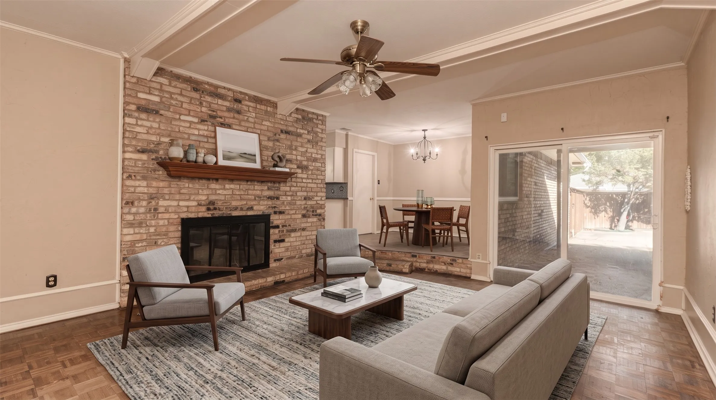 Brick-clad fireplace with wood mantle, wood-finish parquet flooring, ceiling fan with integrated lighting, exposed ceiling beams, and sliding glass patio door