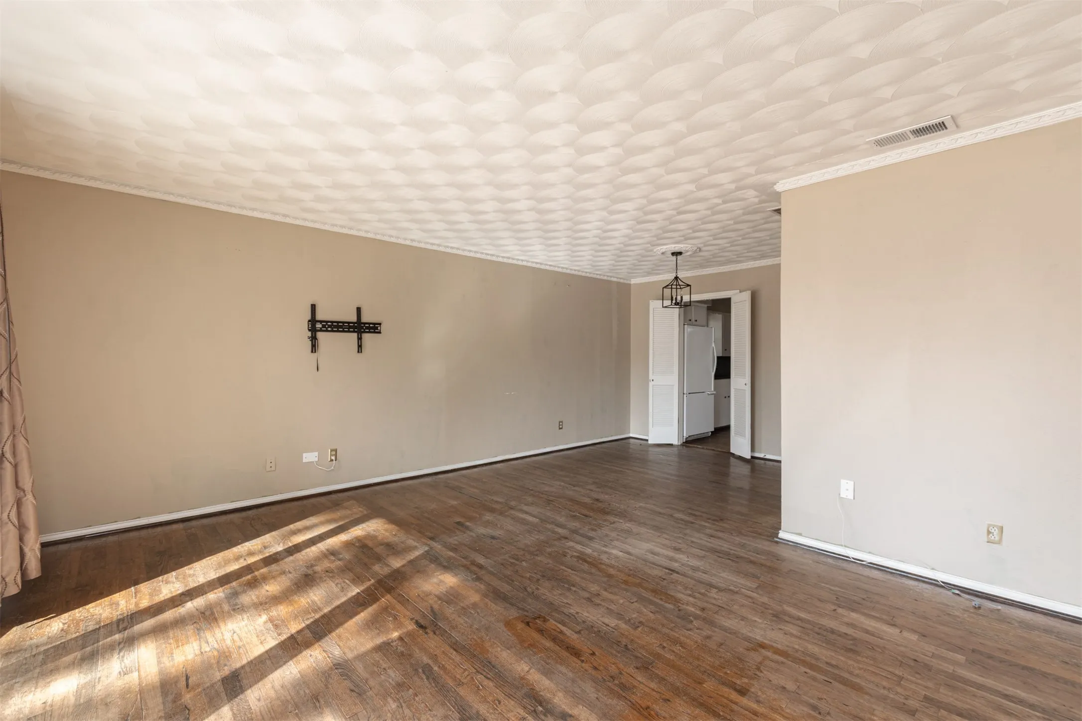 Hardwood flooring, textured ceiling, crown molding, wall-mounted light fixture, and white bi-fold doors