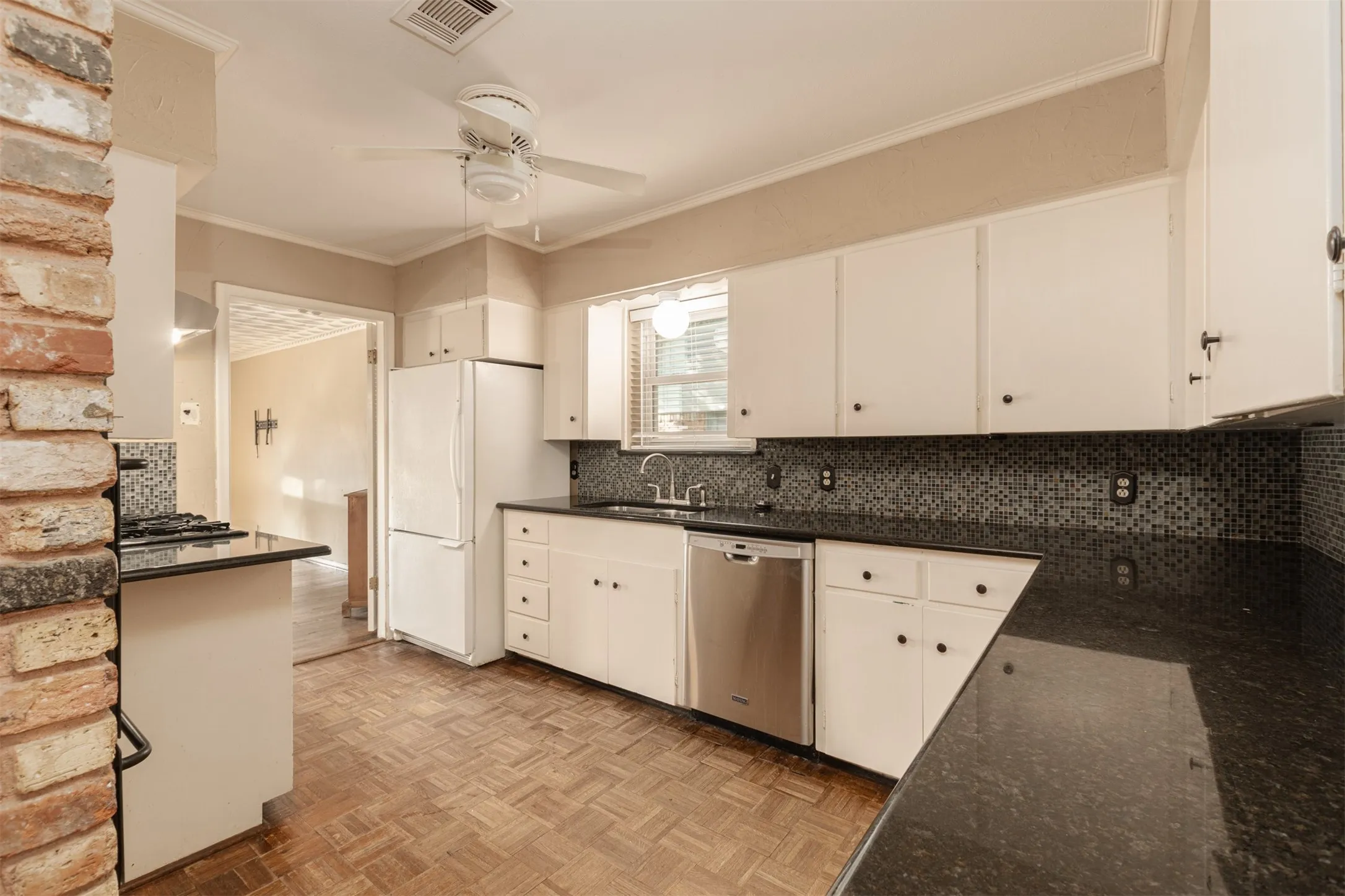 Kitchen with white upper and lower cabinetry, dark countertops, dark mosaic tile backsplash, and parquet wood-finish flooring