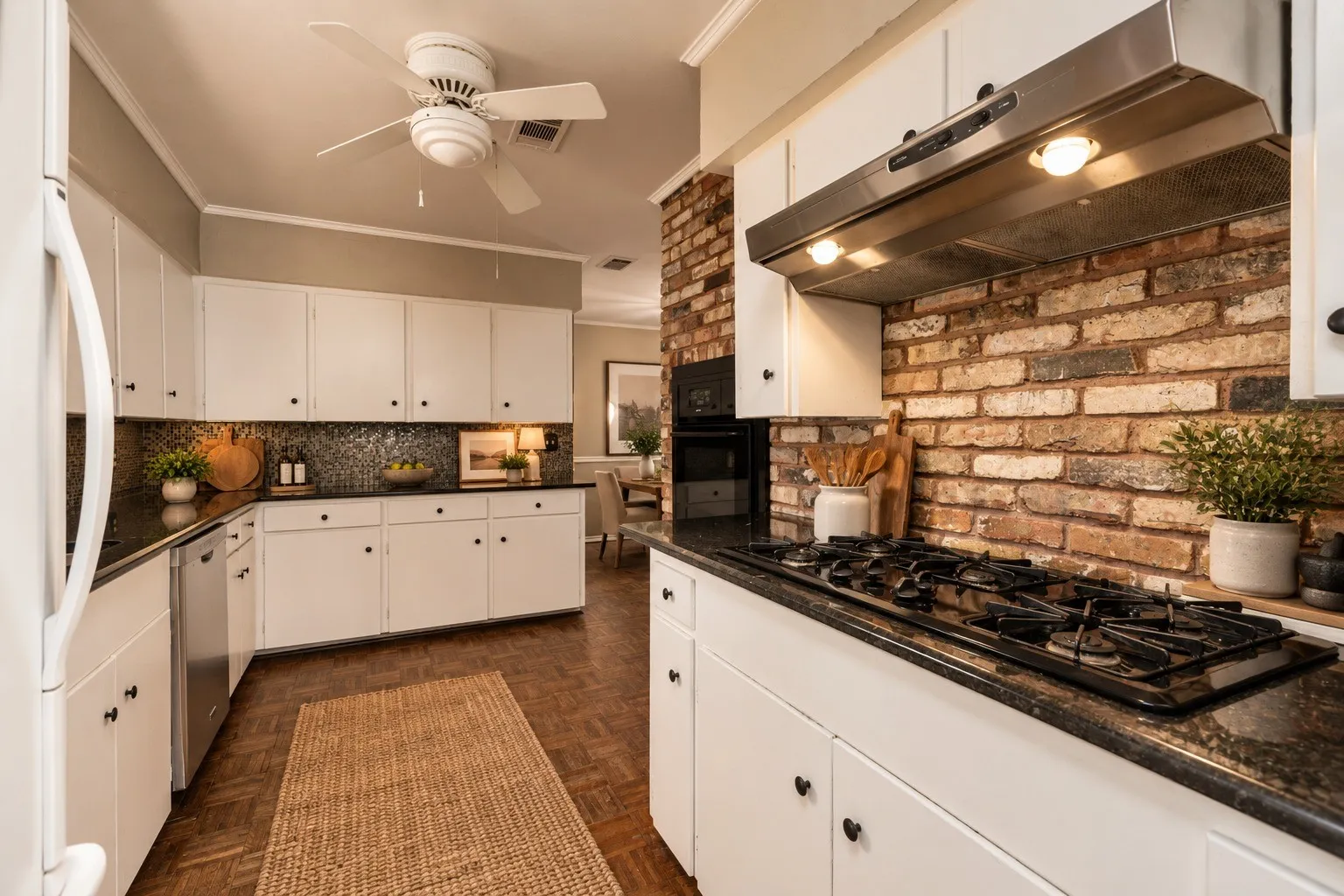 White cabinetry with black hardware, dark countertops, brick backsplash, ceiling fan, and wood-finish flooring