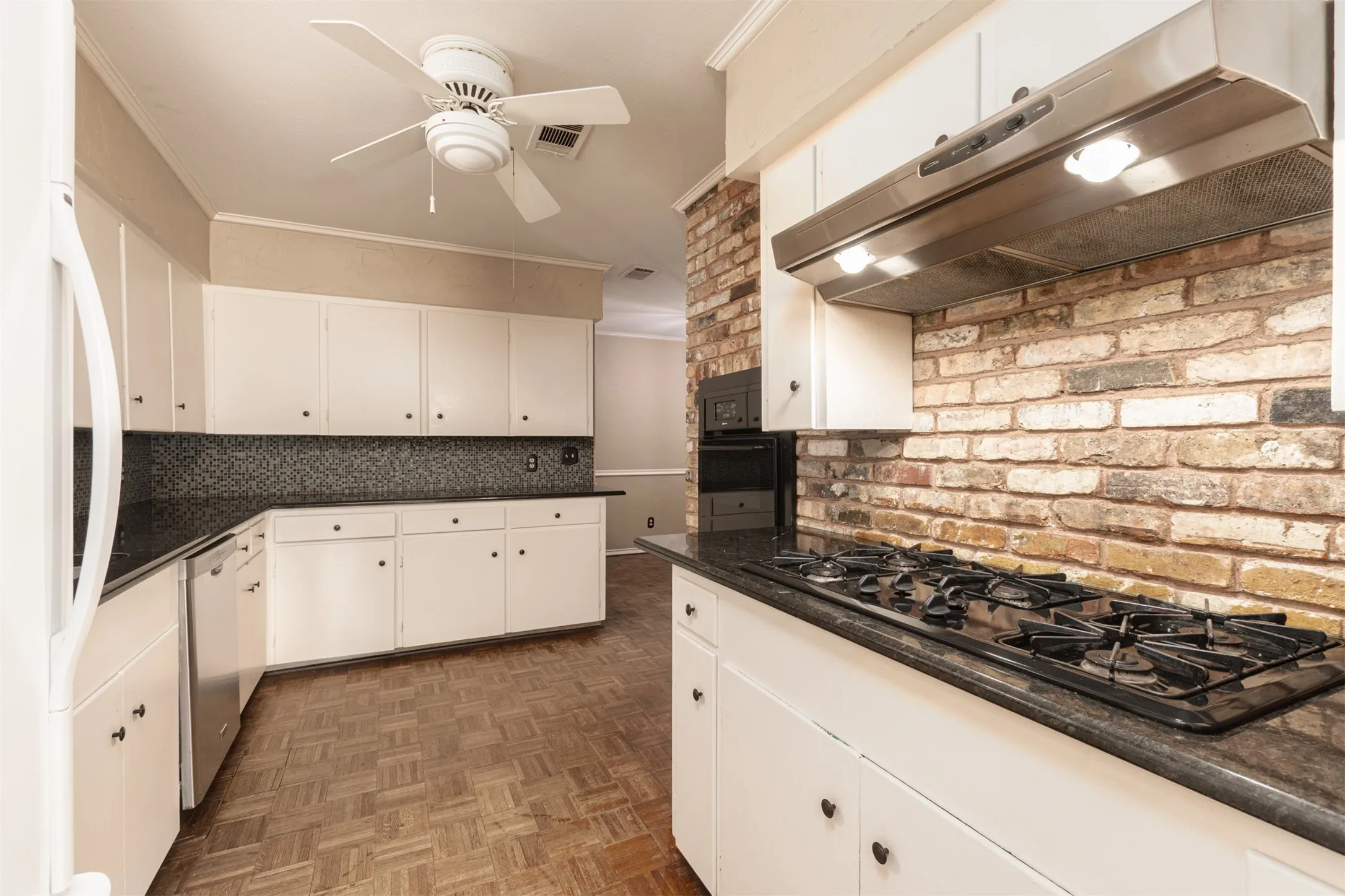 Kitchen featuring white cabinetry, dark countertops, a brick-style backsplash, a gas cooktop, and a stainless steel range hood